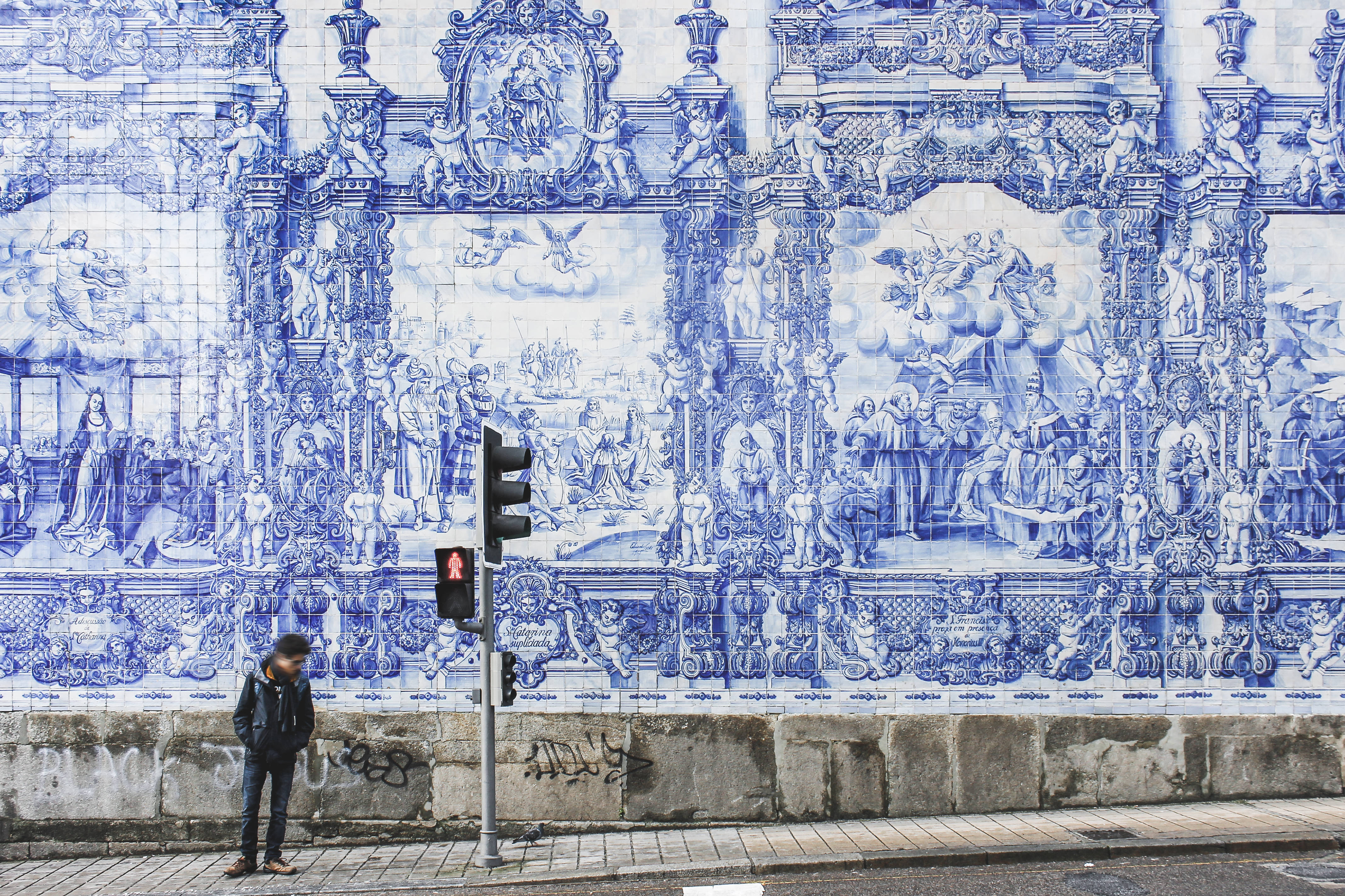 Portugal 桌布 壁紙 — 一個人在城市街道上，在一個描繪宗教場景的巨大華麗藍白瓷磚牆前等待紅燈。