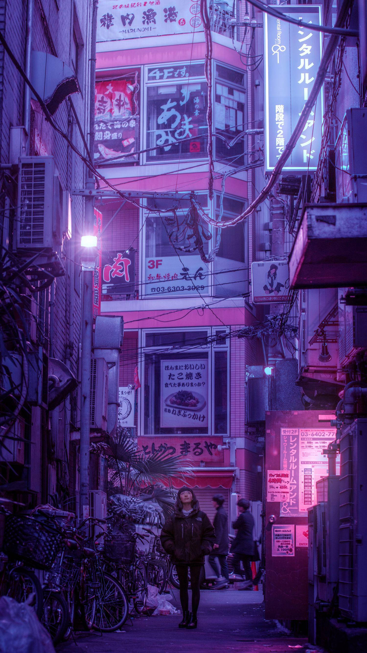 日本 桌布 壁紙 — 一個人在夜晚的東京走下一條狹窄的霓虹燈小巷，周圍是發光的招牌和堆疊的建築物。