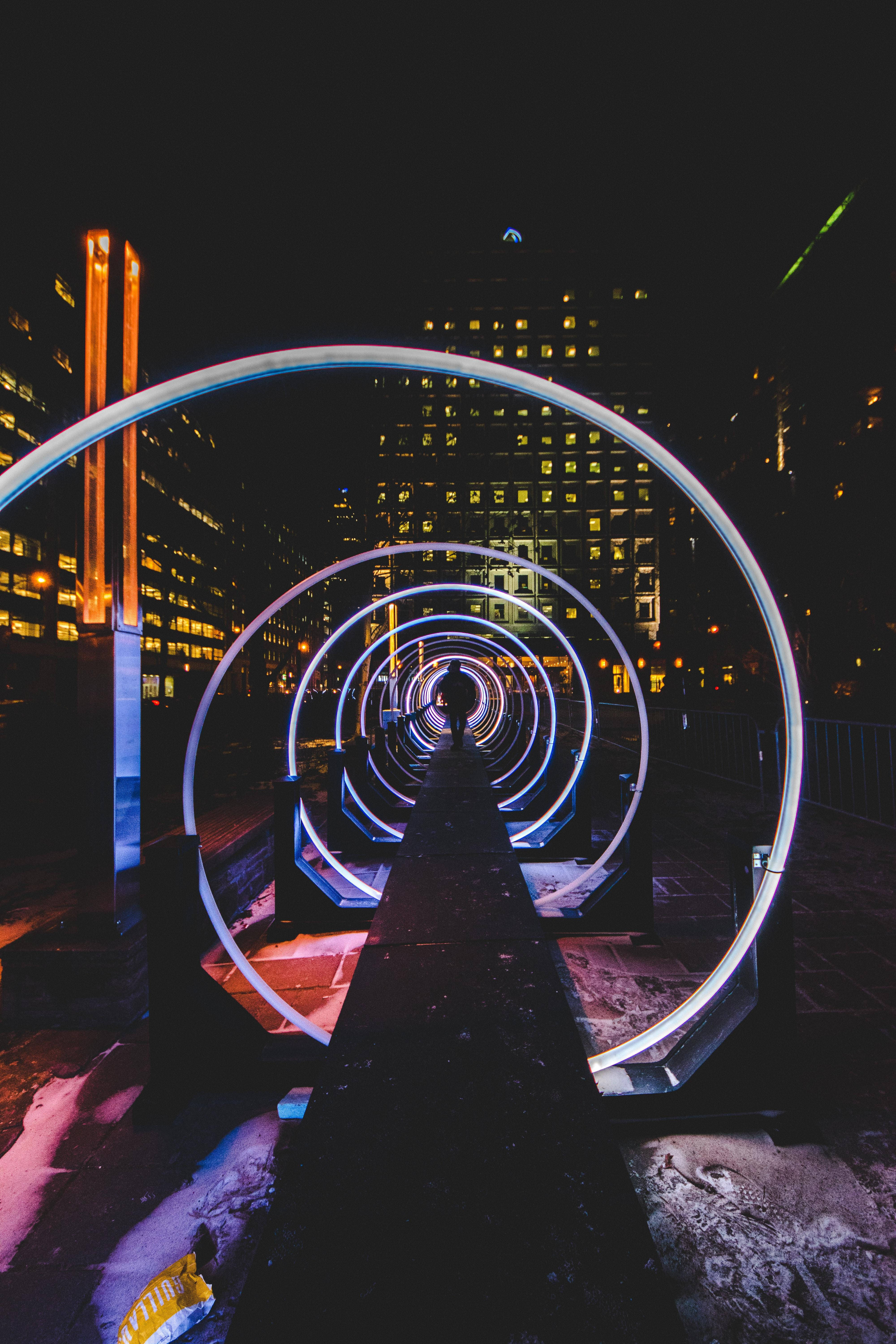 Spiral 桌布 壁紙 — 一個人在夜晚穿過發光的霓虹環，背景是積雪的城市和亮燈的摩天大樓。