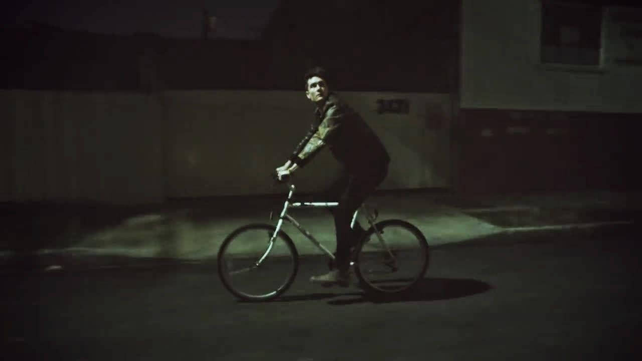 Bastille 桌布 壁紙 — 一個人在夜間黑暗的城市街道上，在單一聚光燈下騎自行車。