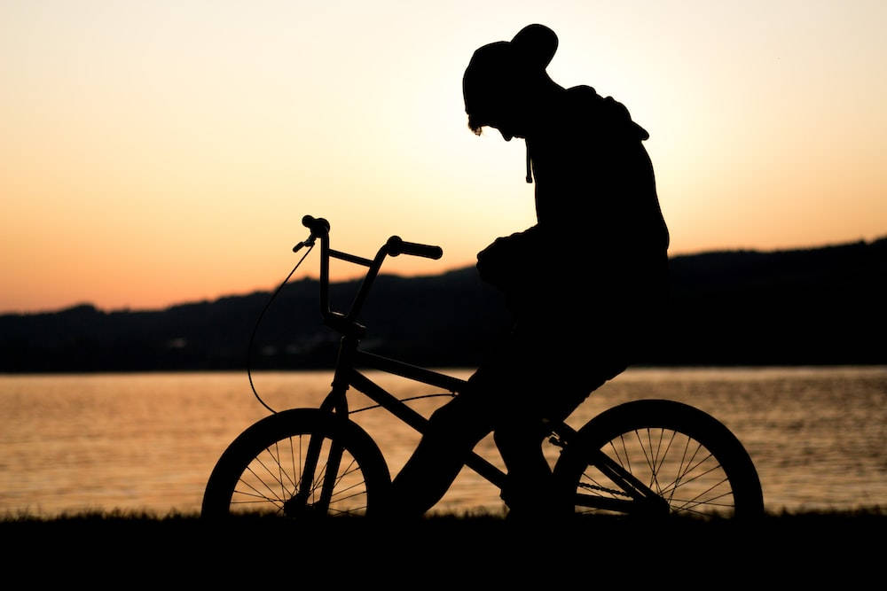 湖邊夕陽下騎腳踏車的人的剪影 — 單身男孩 壁紙