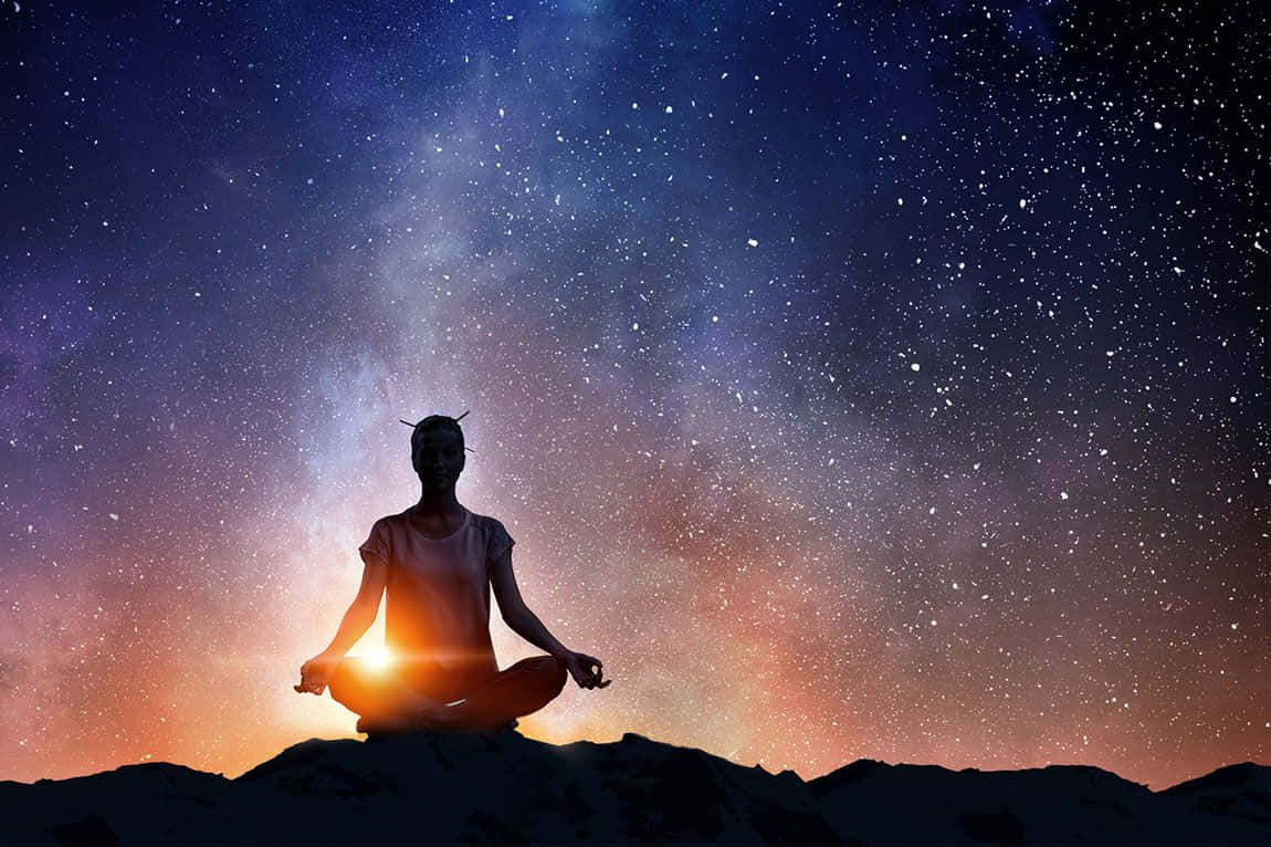 瑜珈 桌布 壁紙 — 一個人在山頂上以剪影形式冥想，背景是充滿活力的星空，帶有發光的宇宙色調。