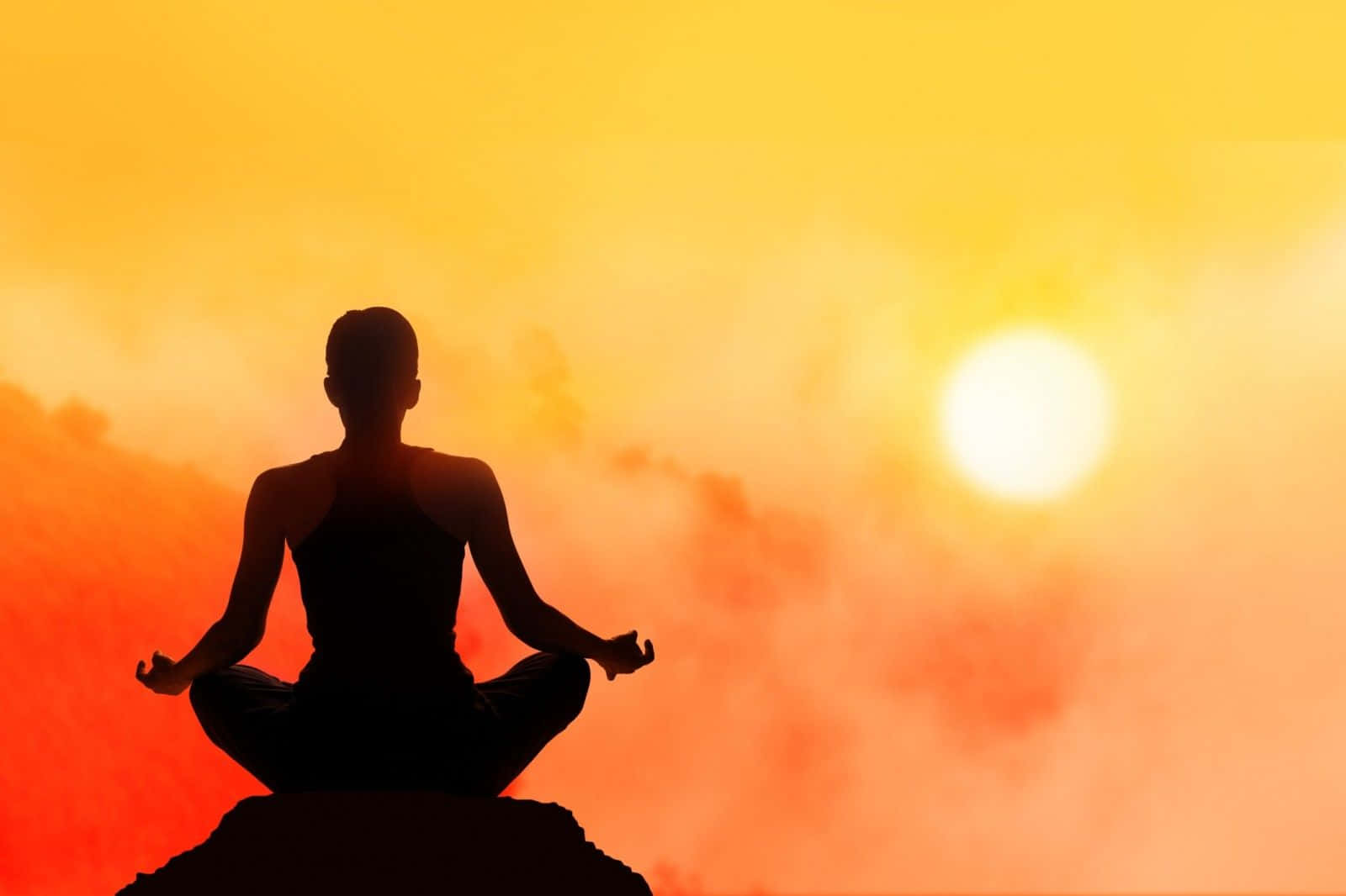 Transcendental 桌布 壁紙 — 一個人在岩石上盤腿打坐的剪影，背景是充滿活力的橙色和黃色日落天空。