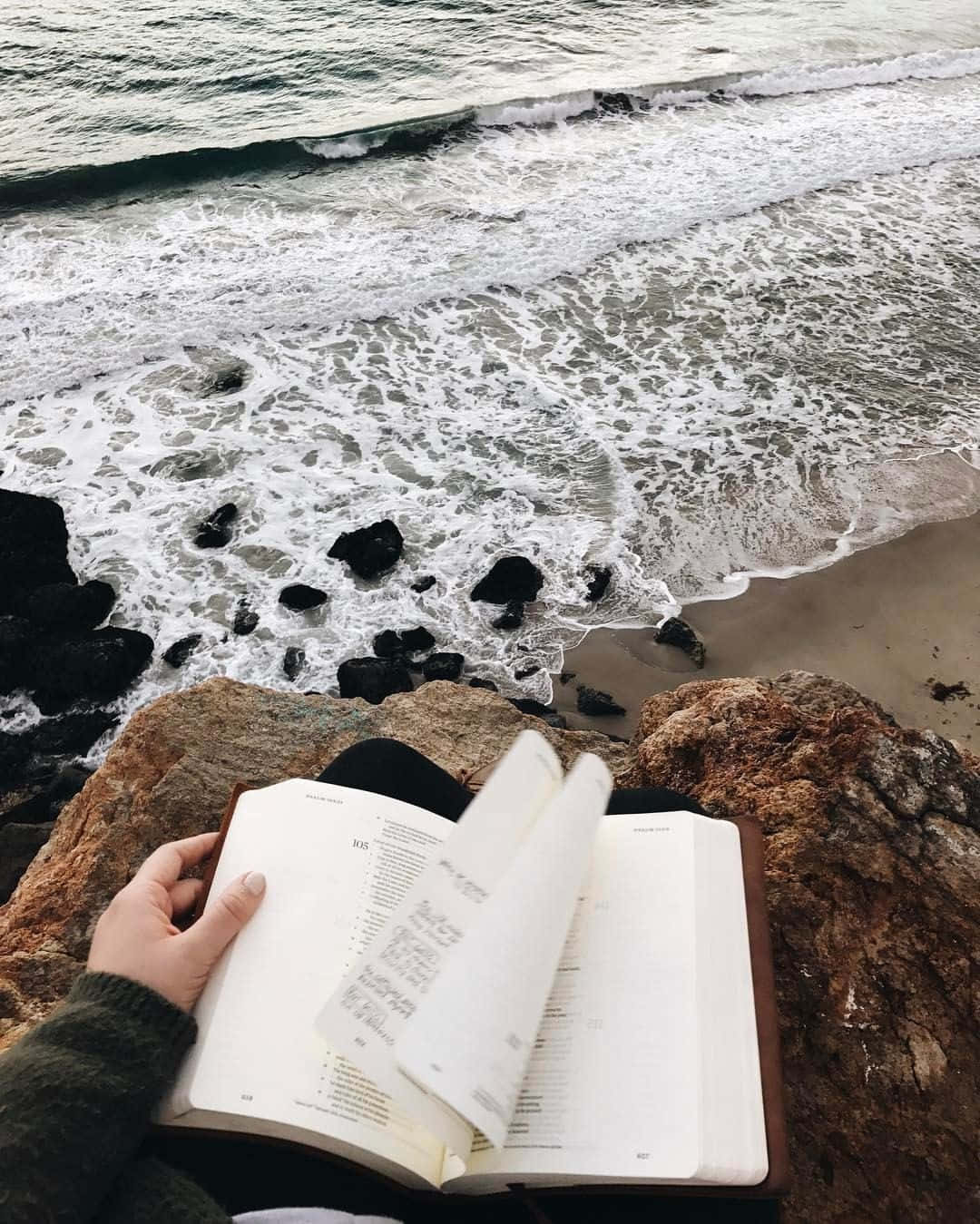 Tumblr 桌布 壁紙 — 一個人在岩石懸崖上閱讀一本書，俯瞰著洶湧的海浪和泡沫般的衝浪。