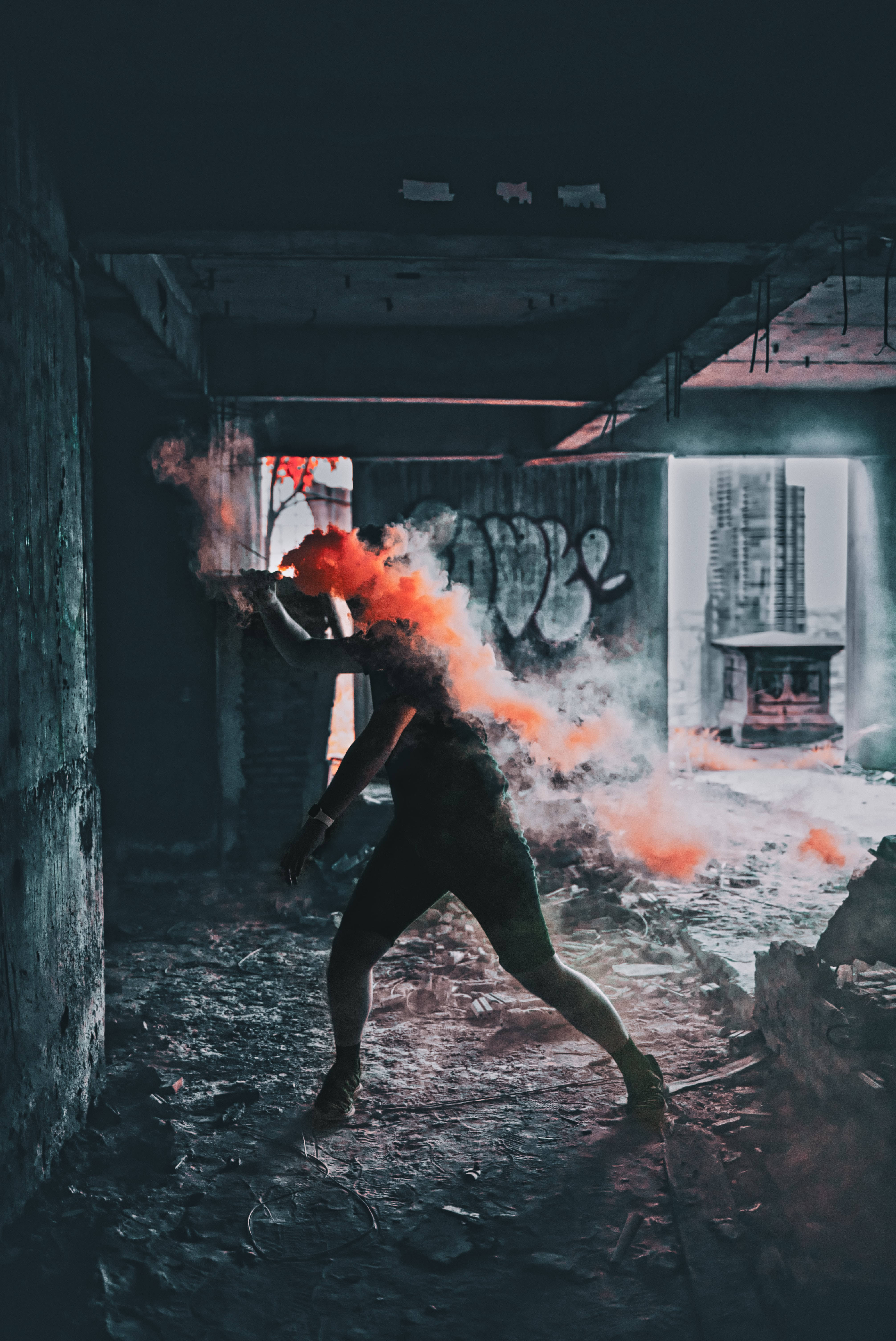 匿名 桌布 壁紙 — 一個人在廢墟建築中，高舉信號彈釋放出鮮豔的橙色煙霧，背景是深色混凝土牆和塗鴉。