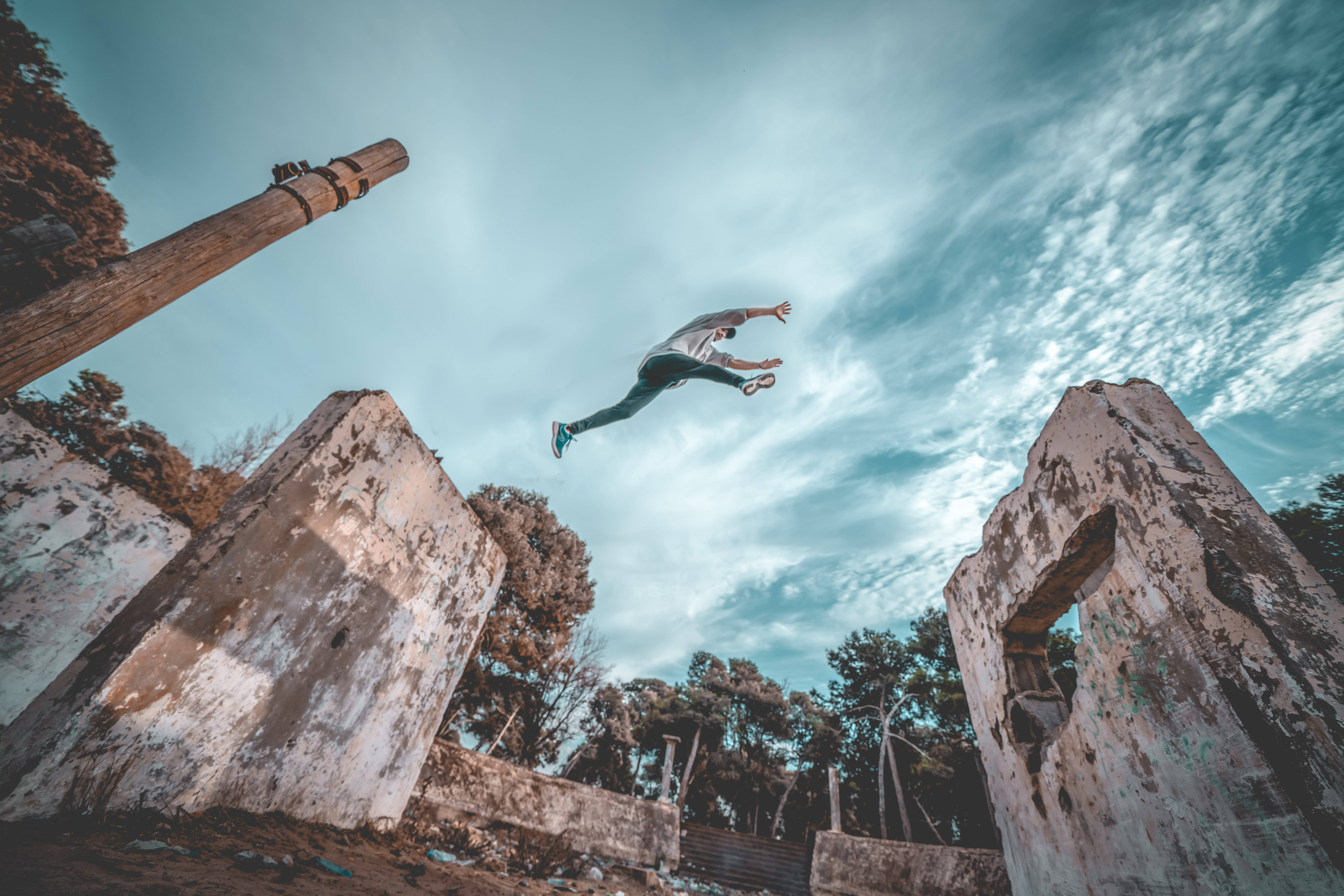 Parkour 桌布 壁紙 — 一個人在廣闊多雲的天空下，在 crumbling 的混凝土廢墟之間凌空飛躍。