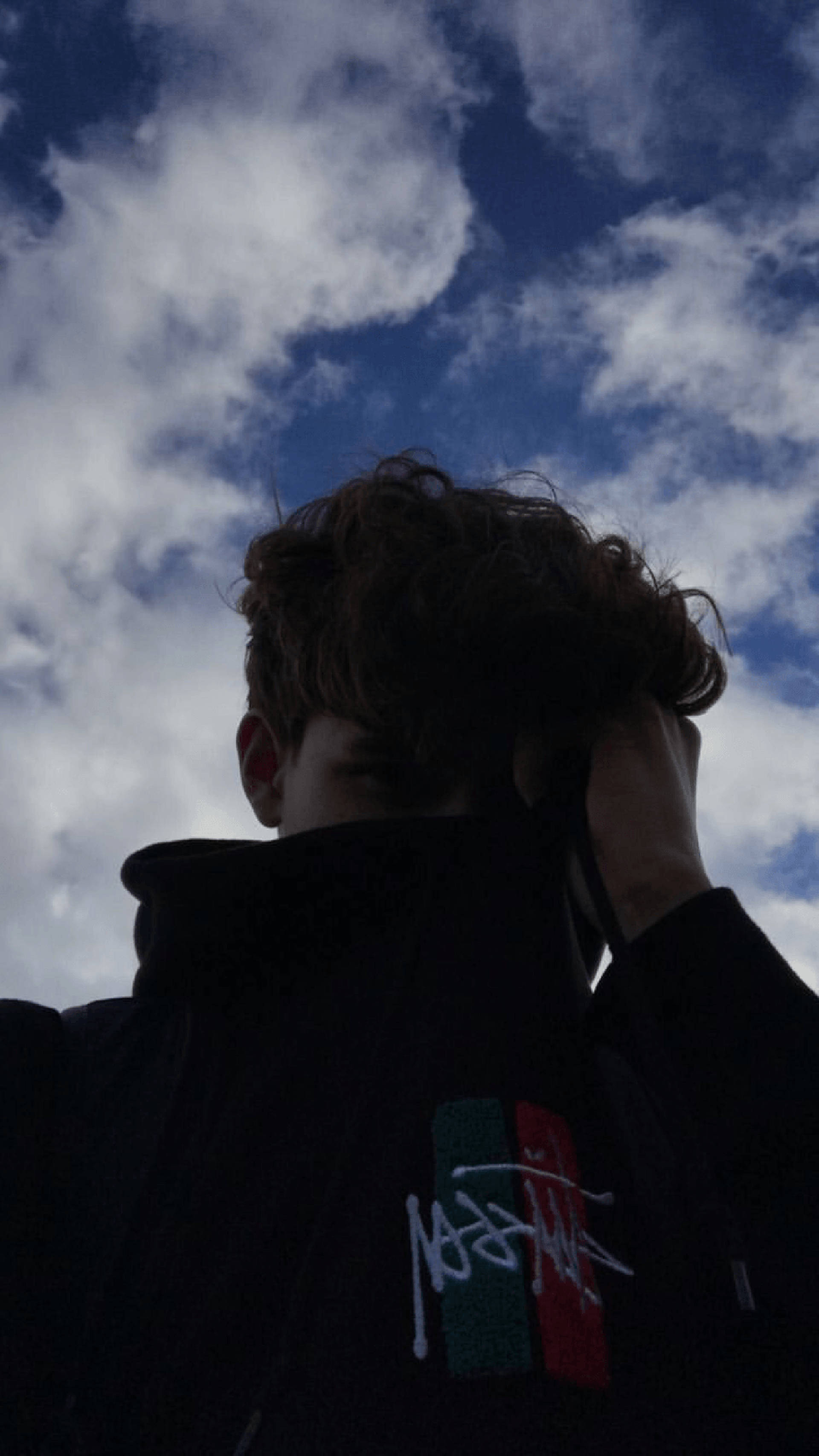美少年動態圖 桌布 壁紙 — 一個人在戲劇性的藍天和蓬鬆的白雲背景下呈現剪影，手舉到頭部。