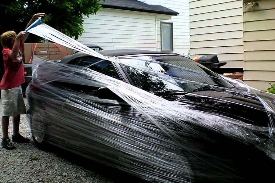 跑車 桌布 壁紙 — 一個人在房屋旁的碎石車道上用透明塑膠膜包裹一輛時尚的黑色跑車。