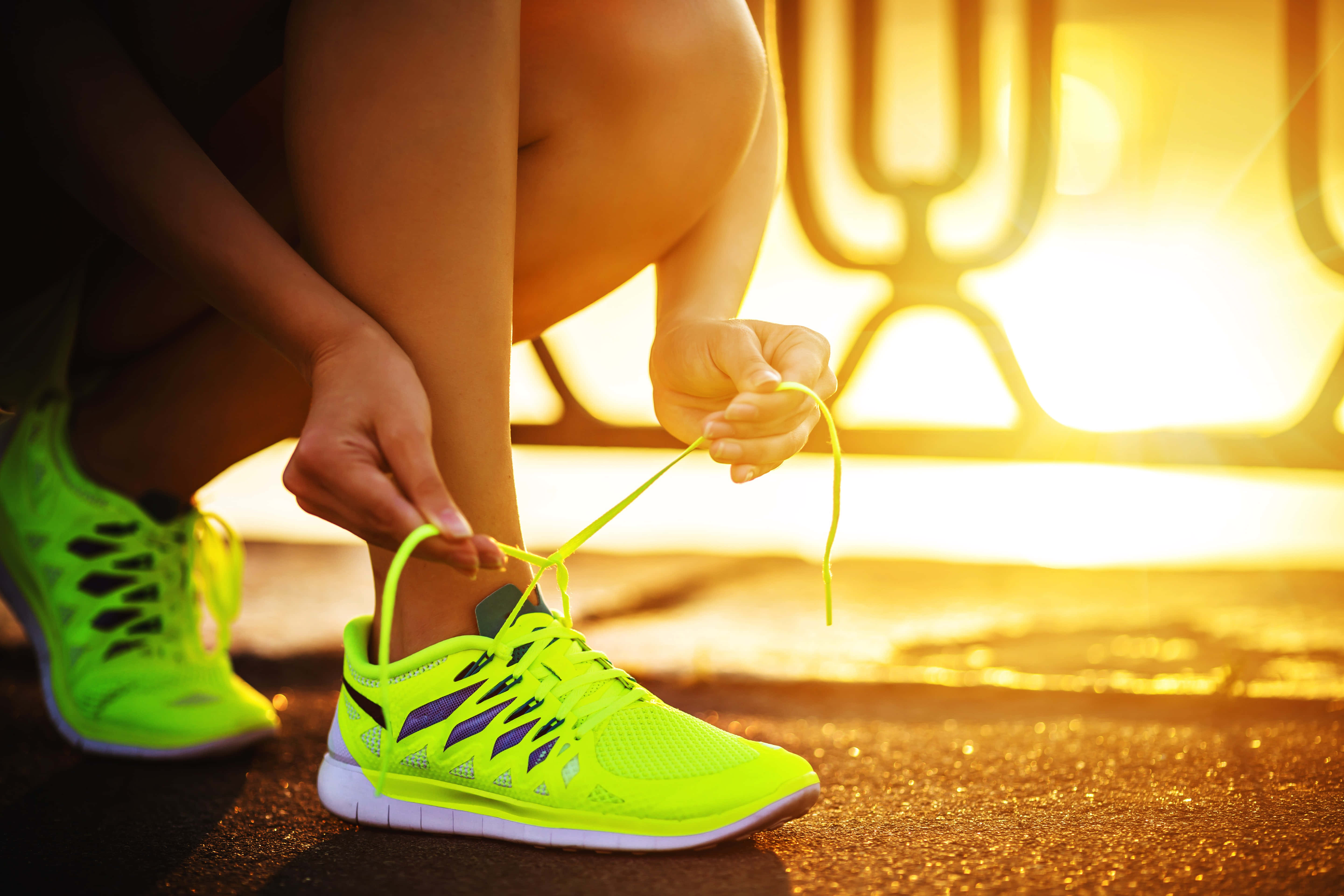 Footwear Design 桌布 壁紙 — 一個人在日出時綁著鮮豔的螢光綠色跑鞋，背後有金色的光芒照耀。