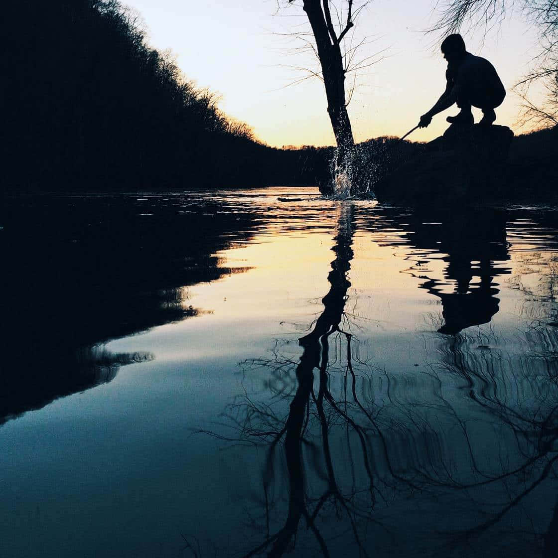 reflection 桌布 壁紙 — 一個人在日落時分從岩石上向平靜的湖面潑水的剪影，湖面映照著樹木的倒影。