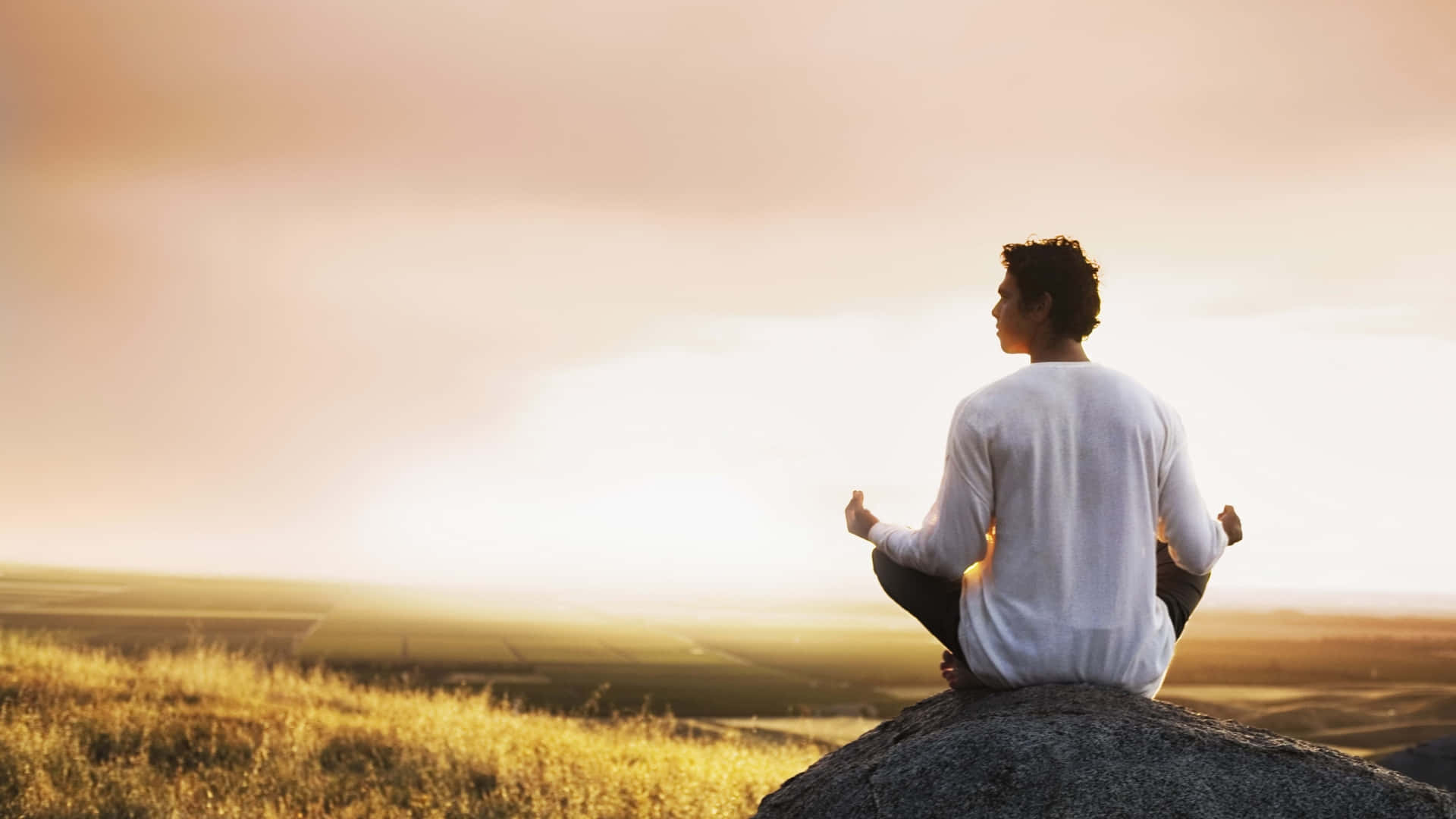 Meditation 桌布 壁紙 — 一個人在日落時分於岩石山丘頂上平靜地冥想，金色光芒沐浴著大地。