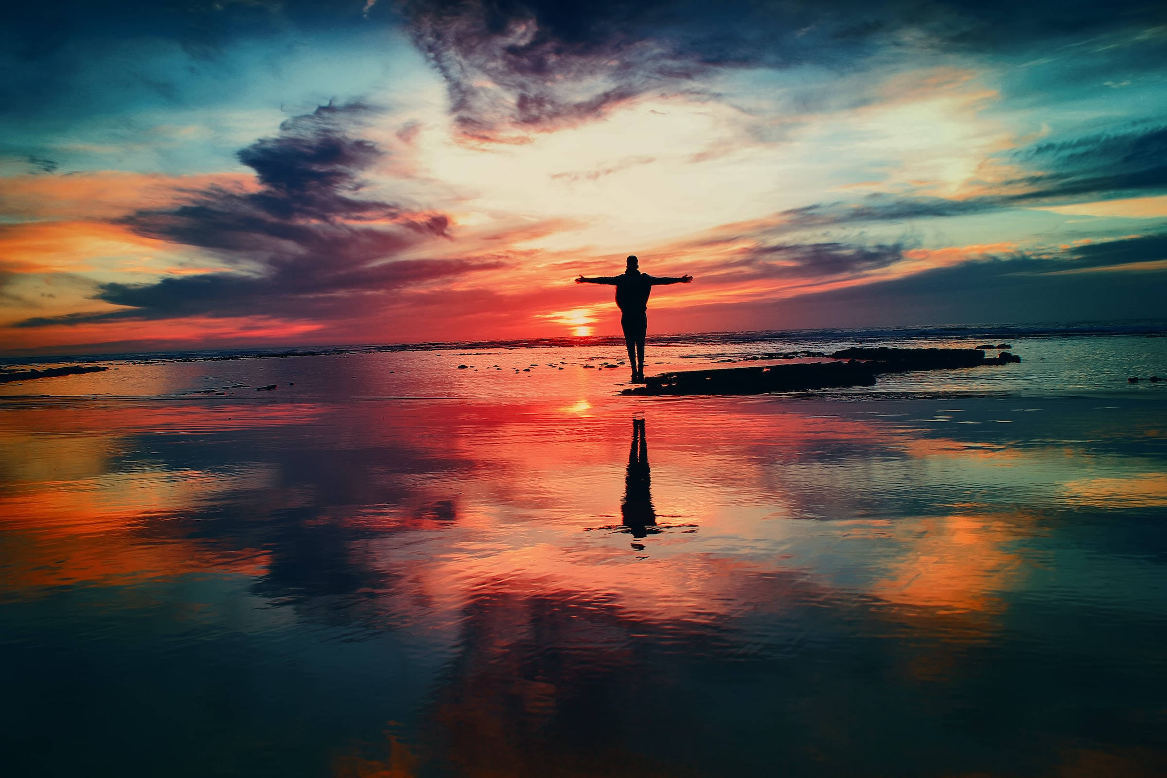 Freedom 桌布 壁紙 — 一個人在日落時分站在岩石上張開雙臂，剪影襯著倒映在平靜水面的火紅天空。