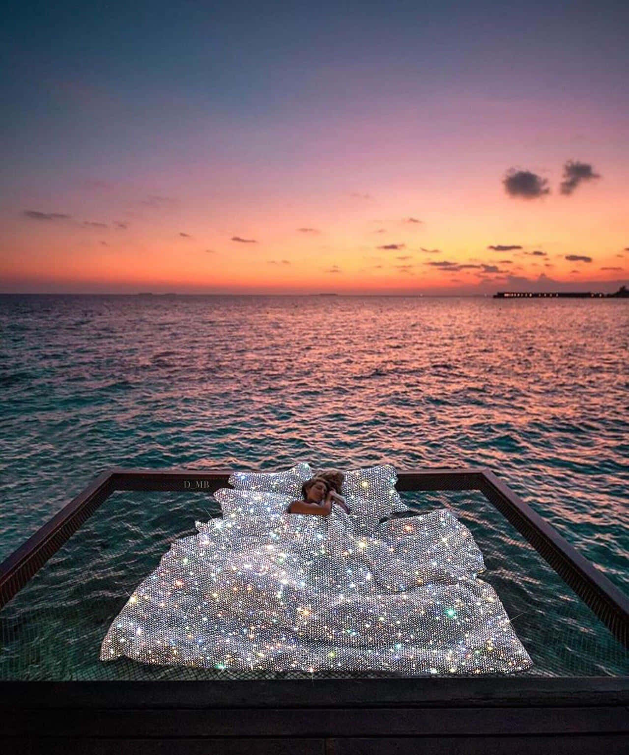 Sunset Beach 桌布 壁紙 — 一個人在日落時分躺在漂浮在海面上的閃爍床上，天空呈現鮮豔的橙色和紫色。