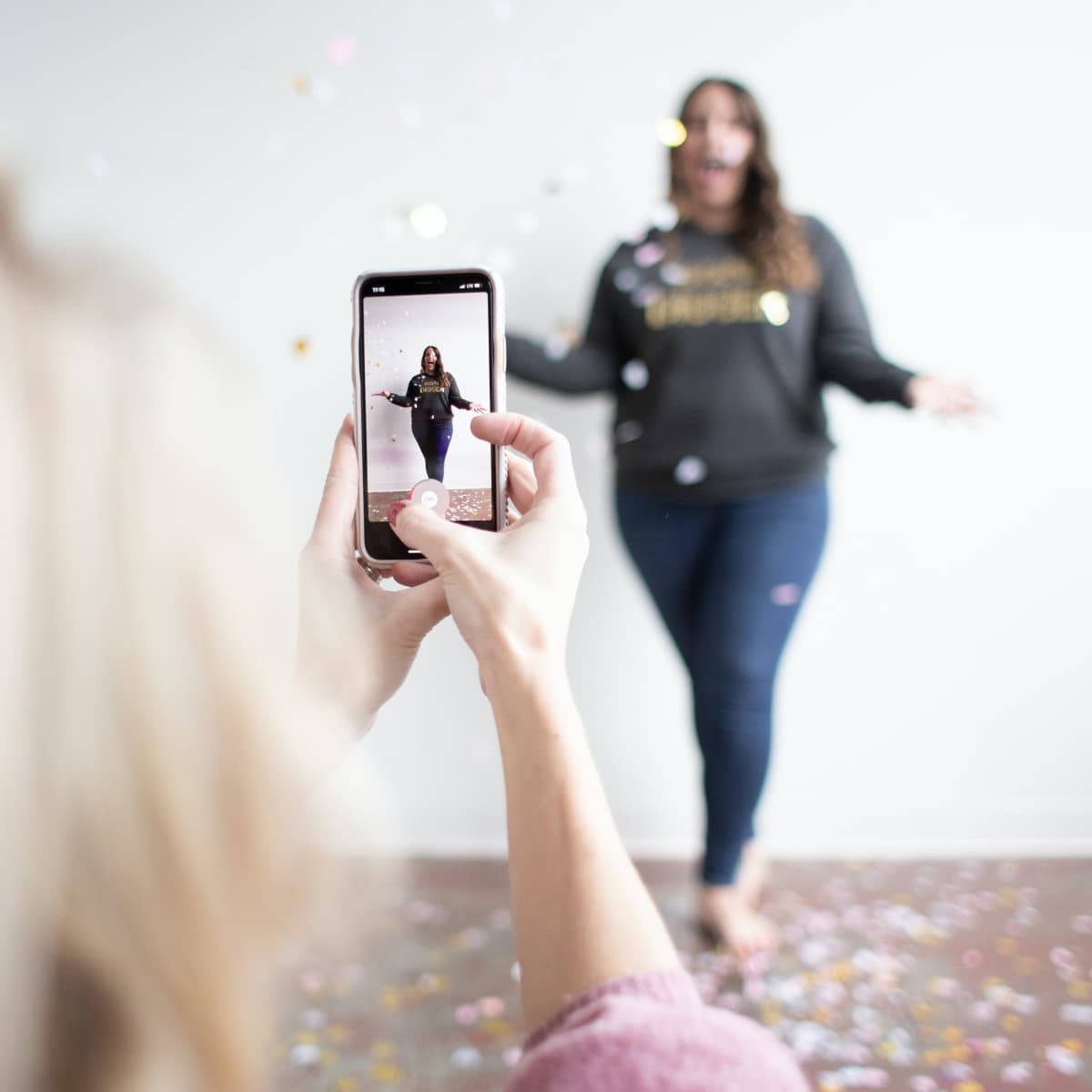 Confetti 桌布 壁紙 — 一個人在明亮的室內空間用智慧型手機捕捉一位快樂的朋友在五彩紙屑中跳舞。