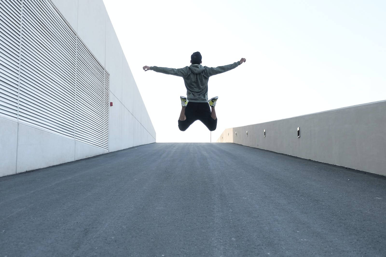 Jumping 桌布 壁紙 — 一個人在明亮的日光下，沿著兩側是純白牆壁的長混凝土走廊，在空中歡快地跳躍。