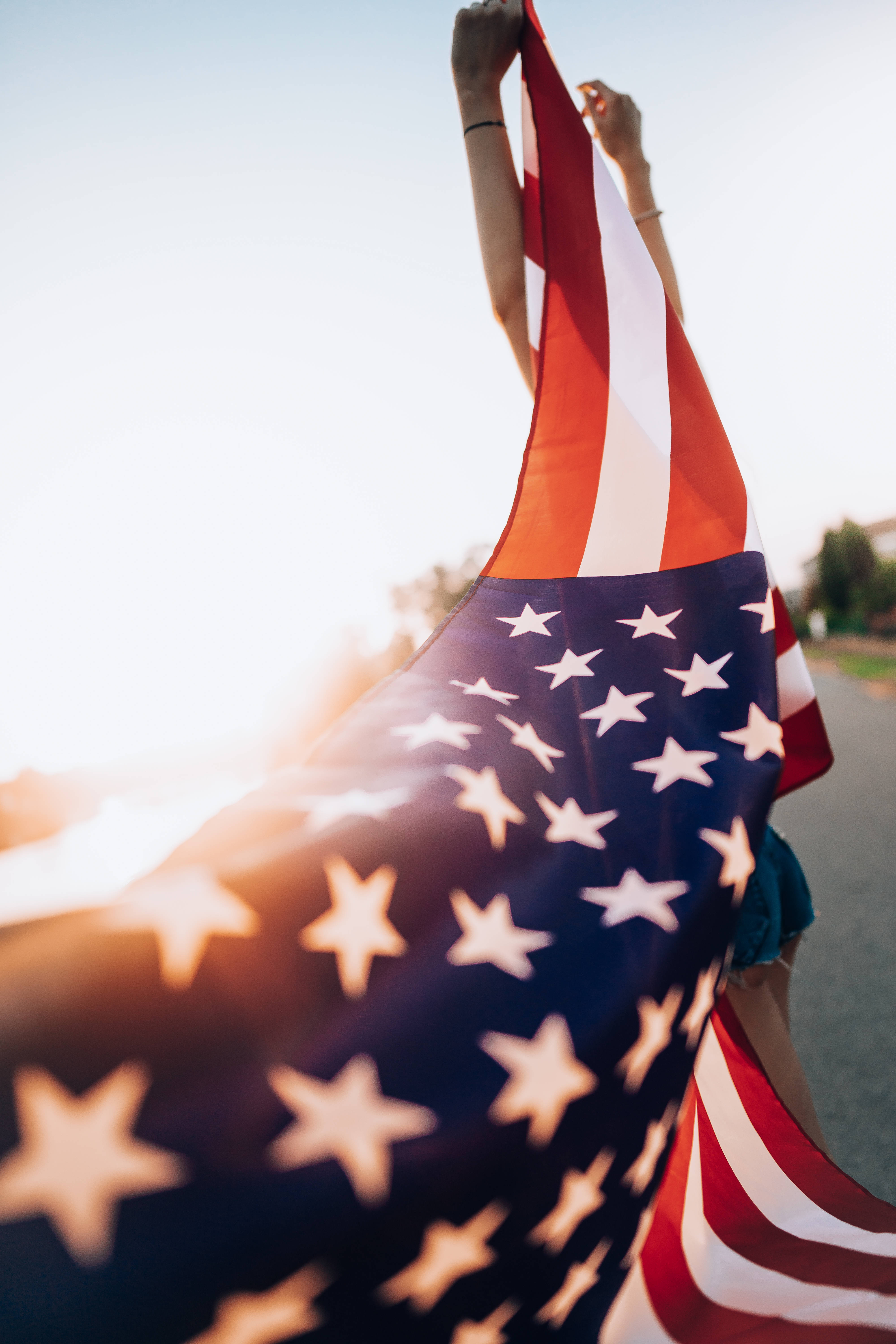 American Flag iPhone 桌布 壁紙 — 一個人在明亮的日落天空下高舉美國國旗，帶有鏡頭光暈。