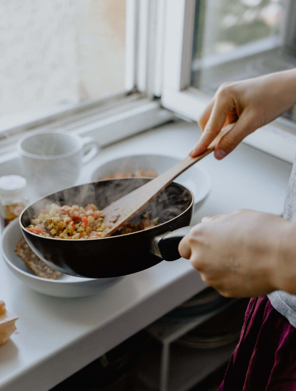 烹飪 桌布 壁紙 — 一個人在明亮的窗台廚房檯上攪拌煎鍋中冒煙的蔬菜。