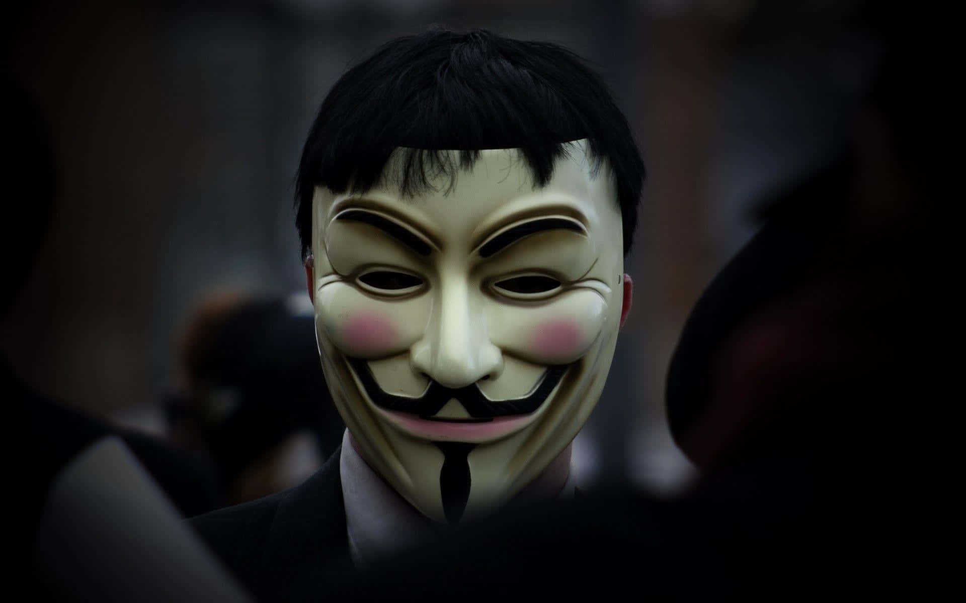 匿名 桌布 壁紙 — 一個人在昏暗的人群中戴著白色 Guy Fawkes 面具，臉頰粉紅，鬍子黑色。