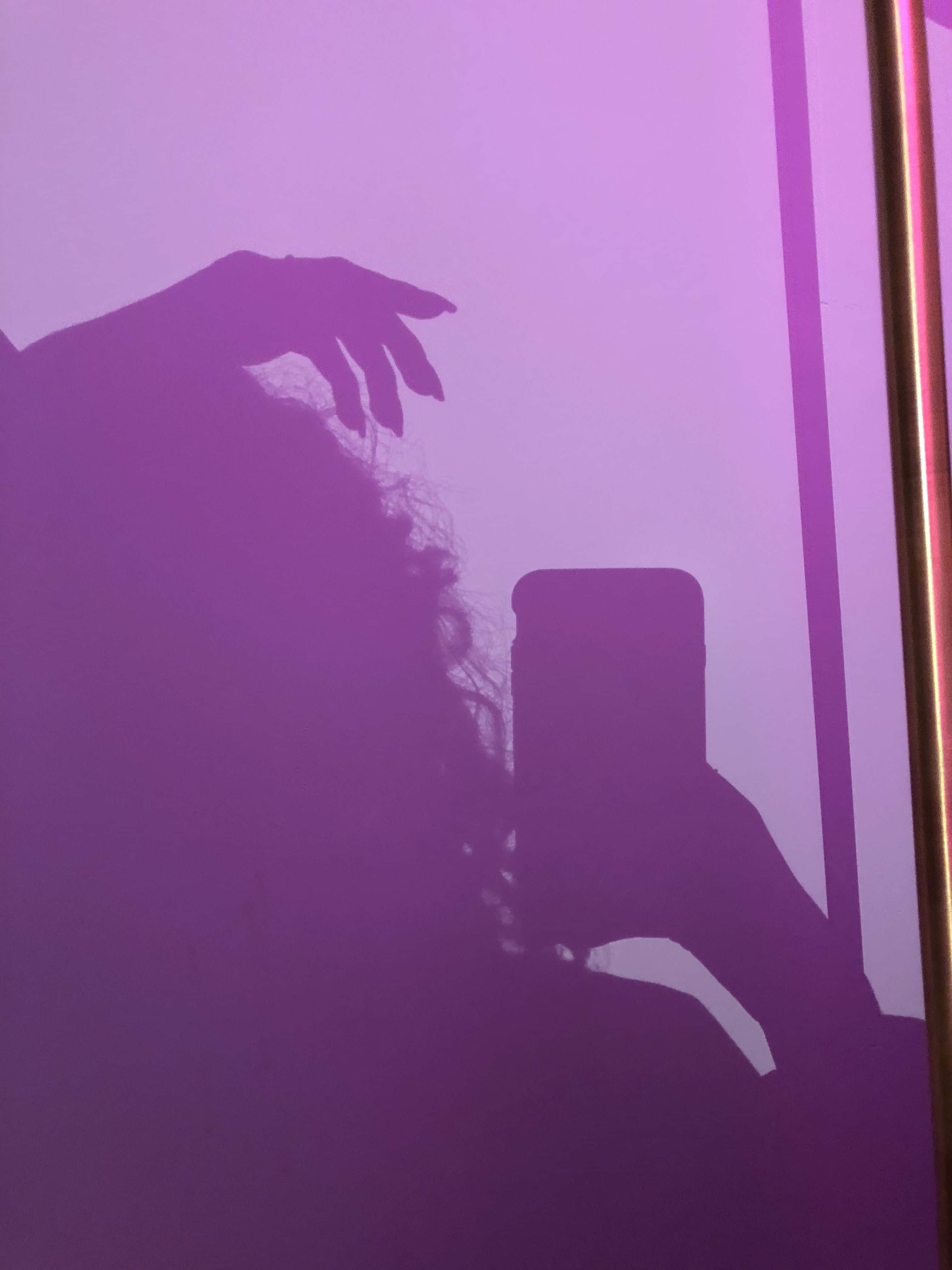 紫色美學 桌布 壁紙 — 一個人在昏暗的房間裏舉起一隻手拿着電話的紫色剪影。