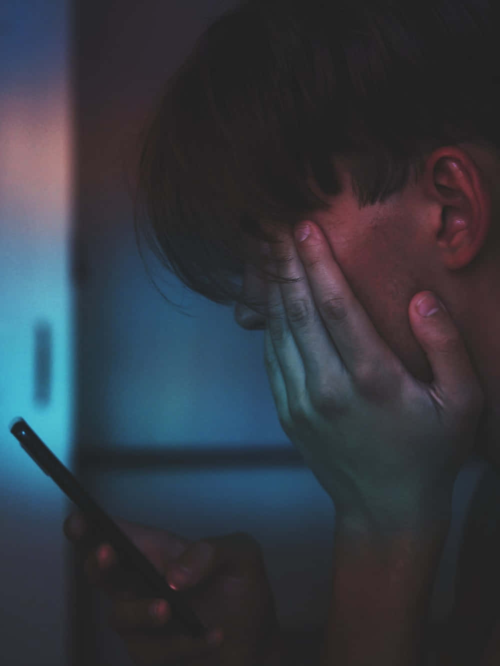 Depressing 桌布 壁紙 — 一個人在昏暗的藍光下用一隻手遮住臉，另一隻手拿著手機。