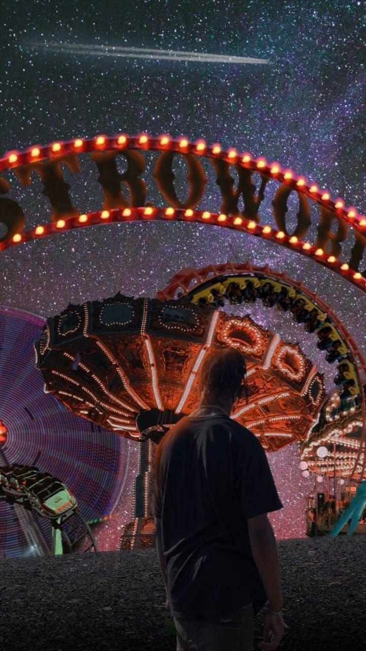 Travis Scott Astroworld 桌布 壁紙 — 一個人在星空下，有流星劃過的嘉年華中，站在發光的「STROWORLD」標誌下方。