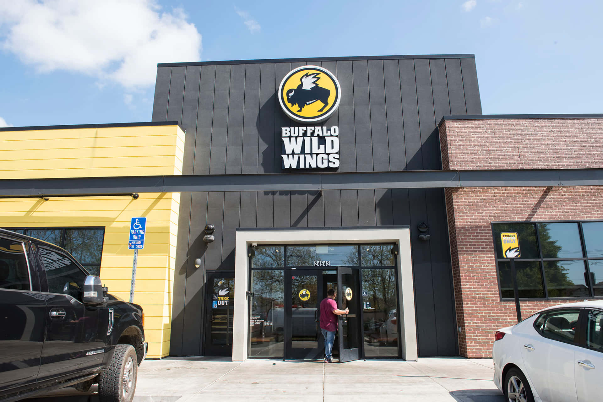 一個人走進 Buffalo Wild Wings 餐廳，外面停著車，陽光明媚。 — 水牛城辣雞翅 壁紙
