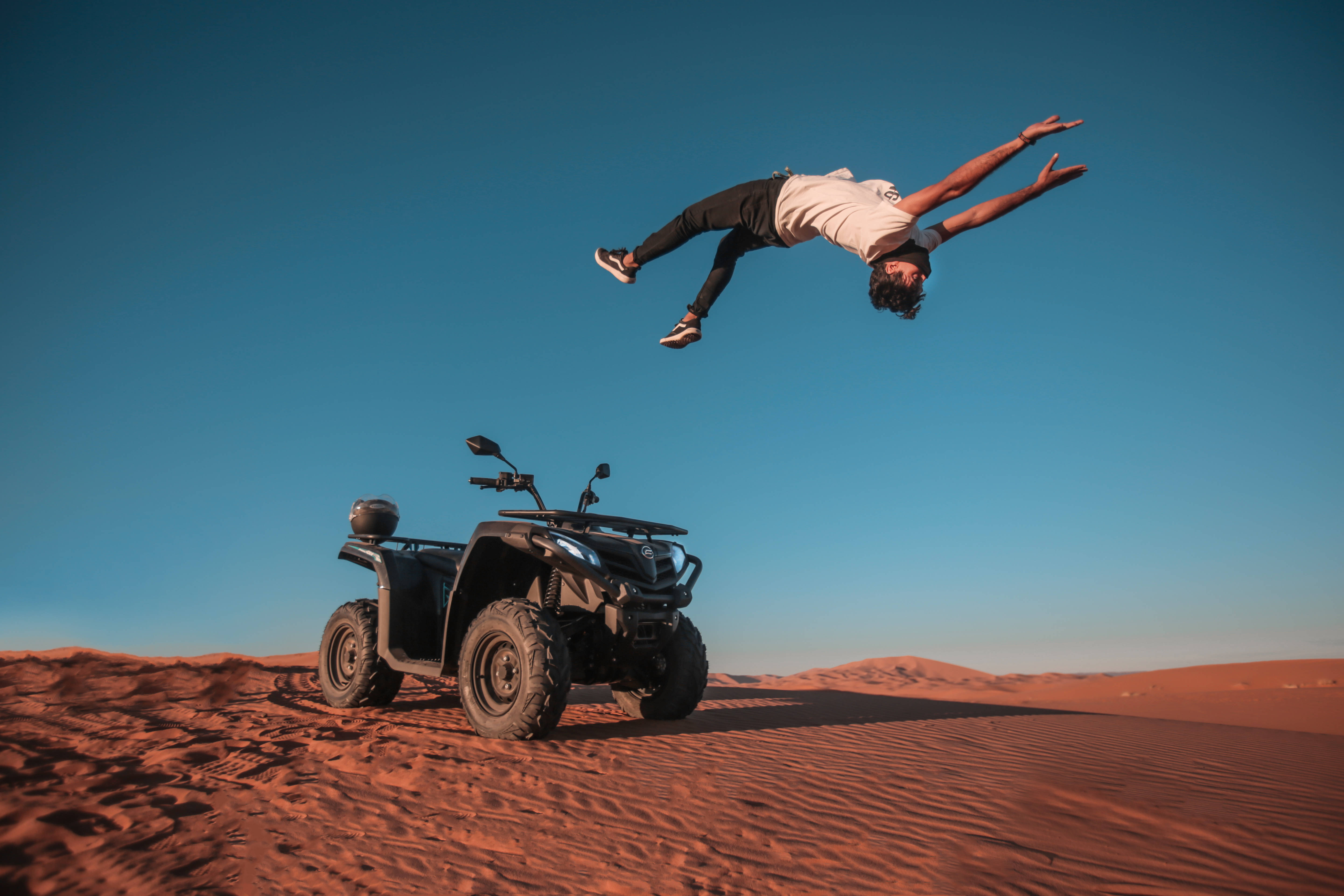 Parkour 桌布 壁紙 — 一個人在晴朗藍天下，在廣闊紅色沙漠中，在停泊的ATV上面做後空翻。
