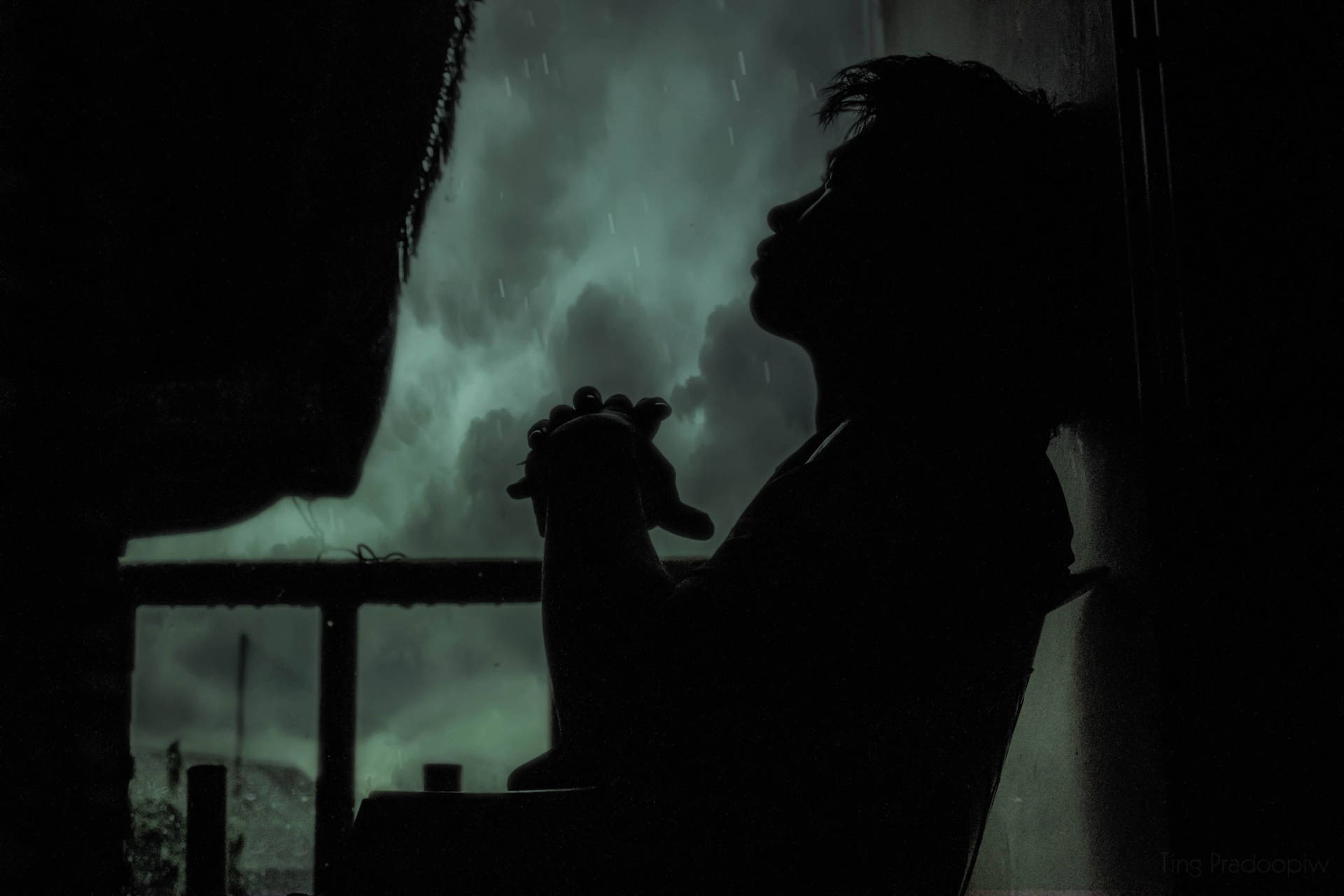 一個人在暴風雨中於下雨的窗邊祈禱的剪影。