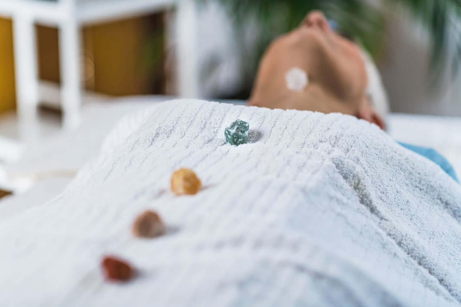 Reiki 桌布 壁紙 — 一個人在有紋理的白色毯子下平靜地休息，彩色石頭排成一排。