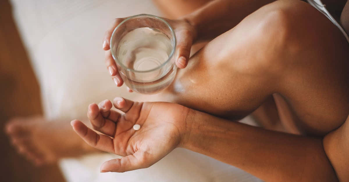 Woman 桌布 壁紙 — 一個人在柔和燈光下，一手拿著一杯水，另一隻張開的手掌上放著一顆藥丸。