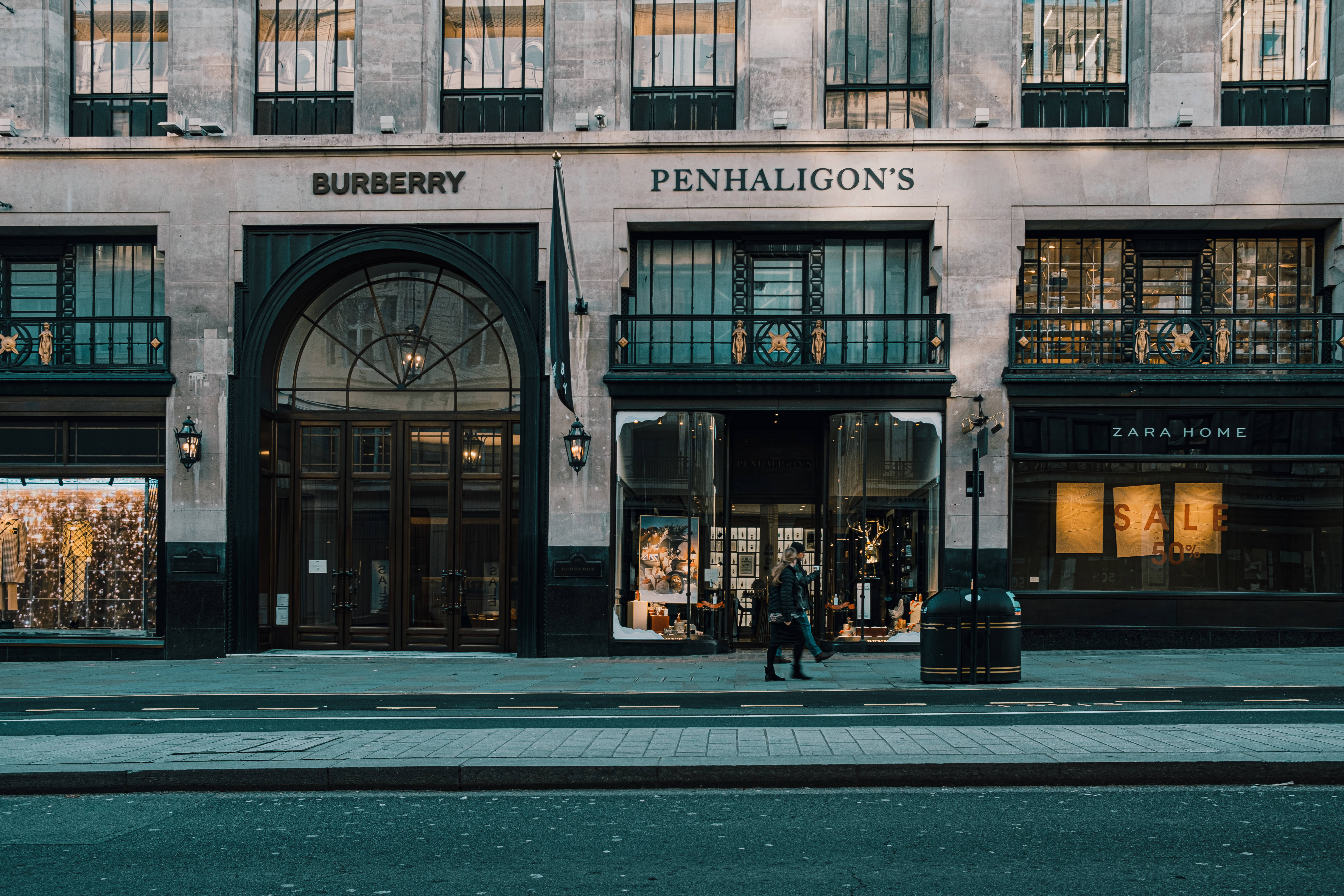 Burberry 桌布 壁紙 — 一個人在柔和的晚燈下走過寧靜的城市街道，經過包括 Burberry 和 Penhaligon's 在內的奢侈品店鋪。