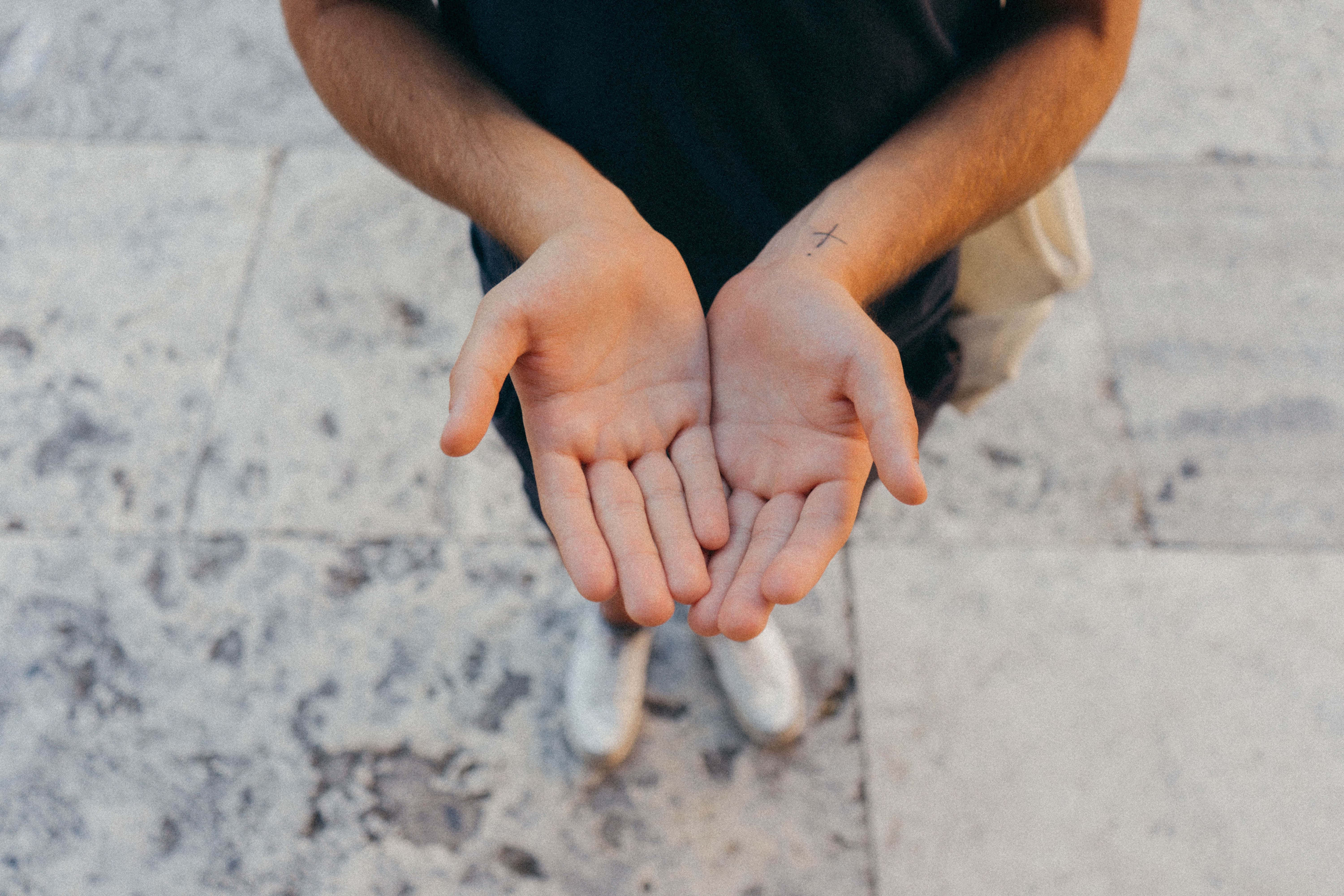 hands 桌布 壁紙 — 一個人在柔和自然光下蹲在石鋪路面上，手掌向上張開。