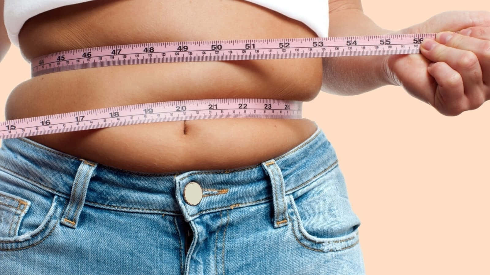 Weight Loss 桌布 壁紙 — 一個人在柔和蜜桃色背景上用粉紅色軟尺測量腰圍。