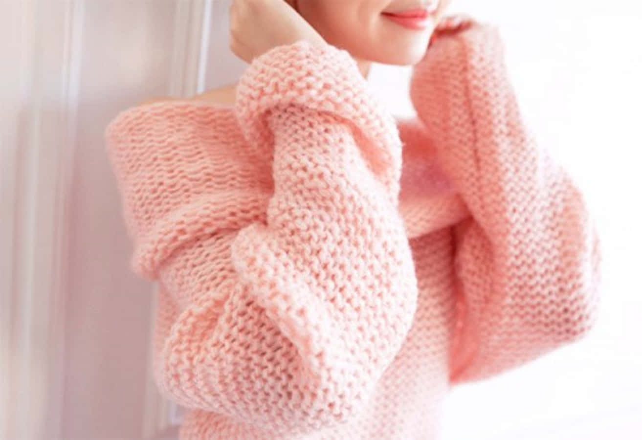 Pink Sweater 桌布 壁紙 — 一個人在柔軟的粉紅色粗針織毛衣中，在舒適的室內環境中輕輕將袖子拉近臉部。