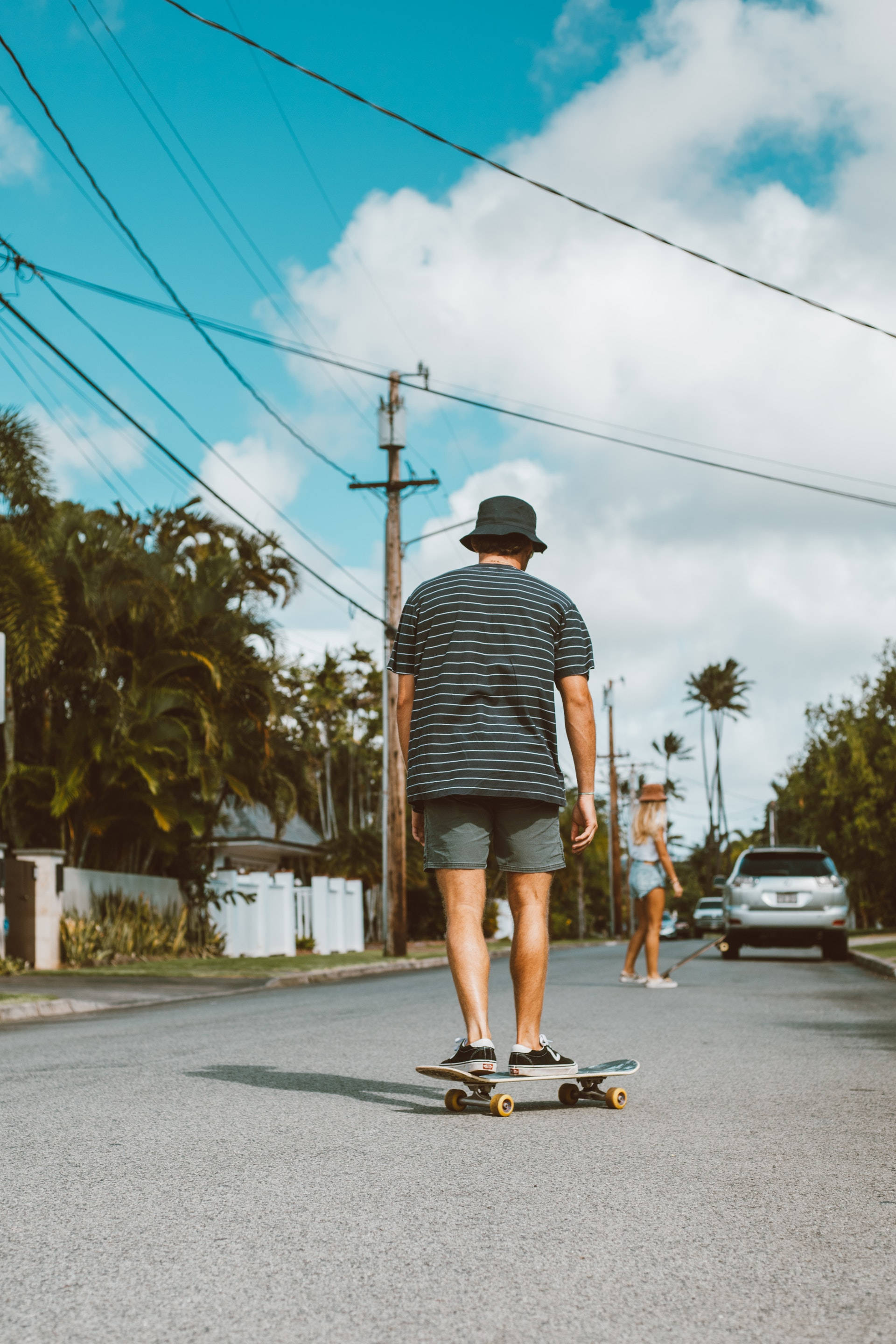 Skater Boy 桌布 壁紙 — 一個人在棕櫚樹成蔭的街道上踩滑板，頭頂是藍天白雲。