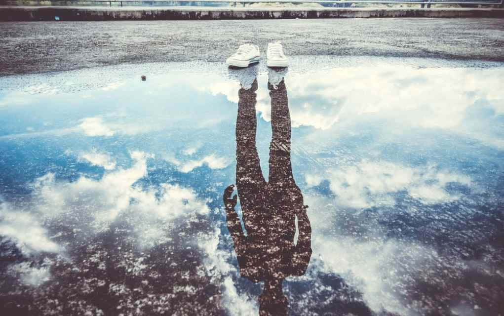 reflection 桌布 壁紙 — 一個人在水坑中的倒影顯示他們的腿和白色運動鞋映照在陰天天空上。