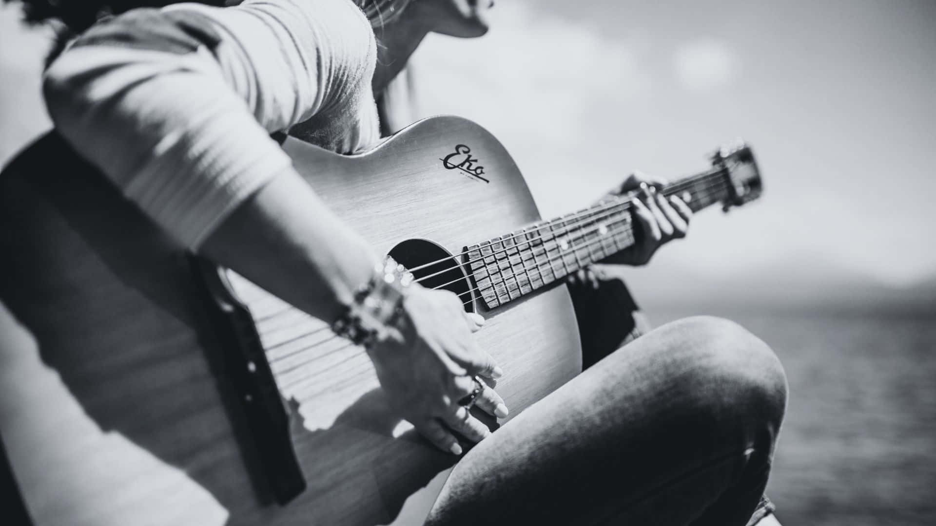 Black And White Guitar 桌布 壁紙 — 一個人在水邊彈奏黑白原聲吉他，柔和陽光灑落。