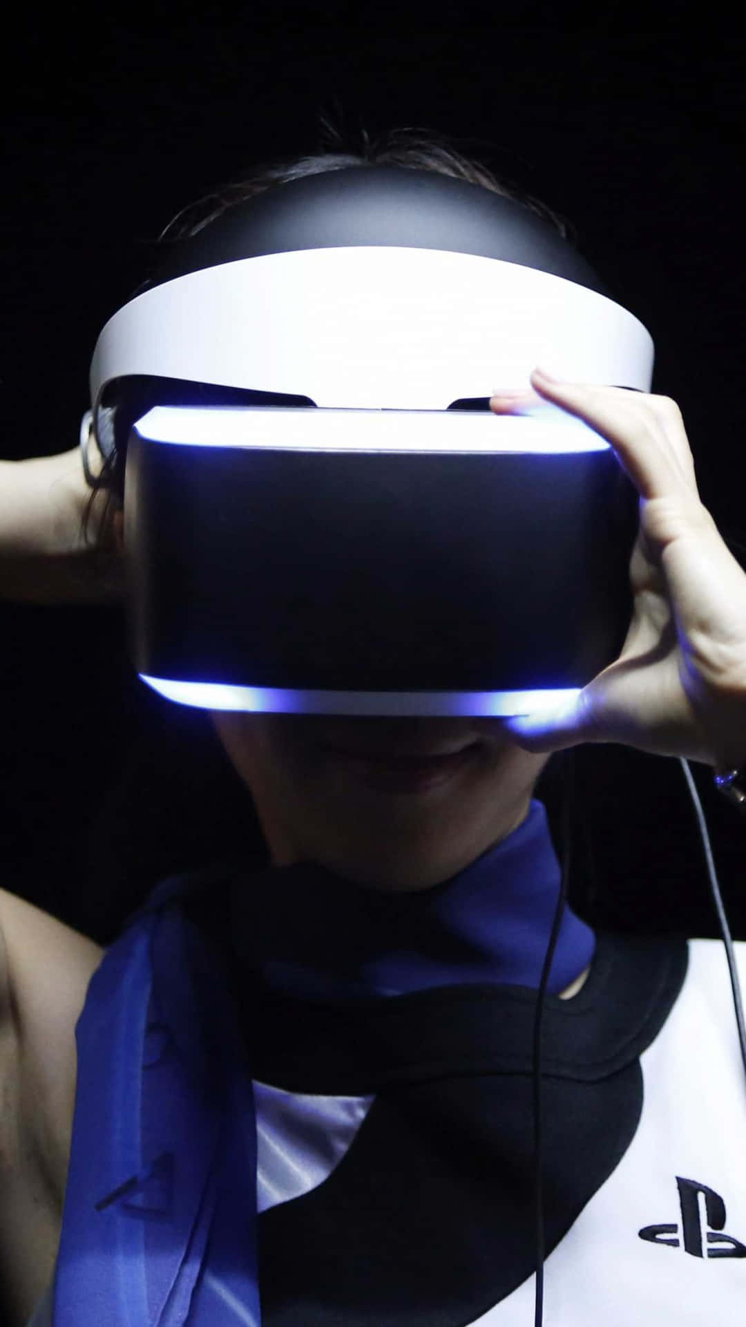 virtual reality 桌布 壁紙 — 一個人在深色背景上調整發光的PlayStation VR頭戴裝置，帶有藍色燈光點綴。