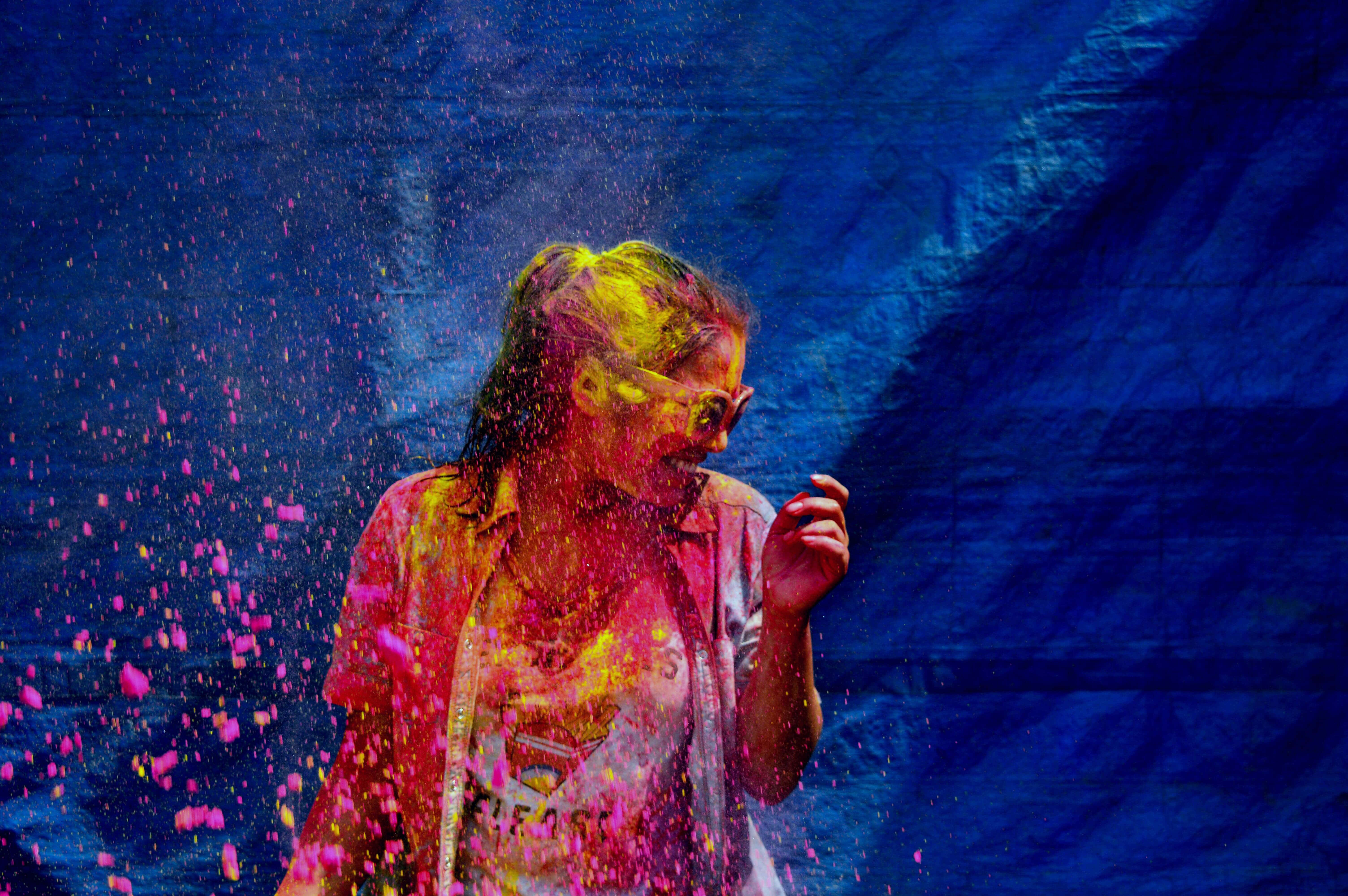 Holi 桌布 壁紙 — 一個人在深藍色背景下，周圍爆發出鮮豔的粉紅色和黃色粉末，開懷大笑。