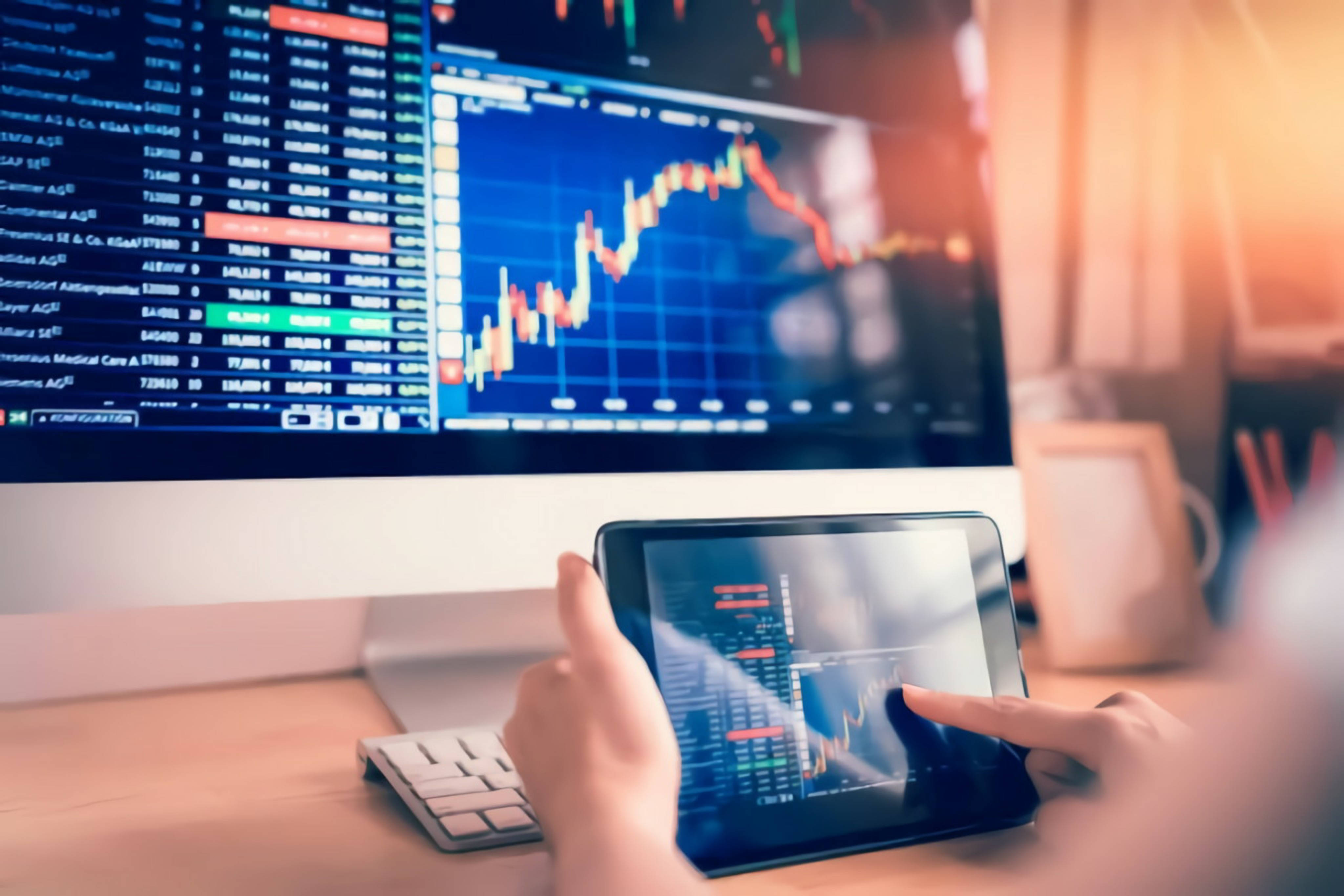 Accounting 桌布 壁紙 — 一個人在溫暖照明的家庭辦公室中，在平板電腦和大顯示器上分析金融股票圖表。