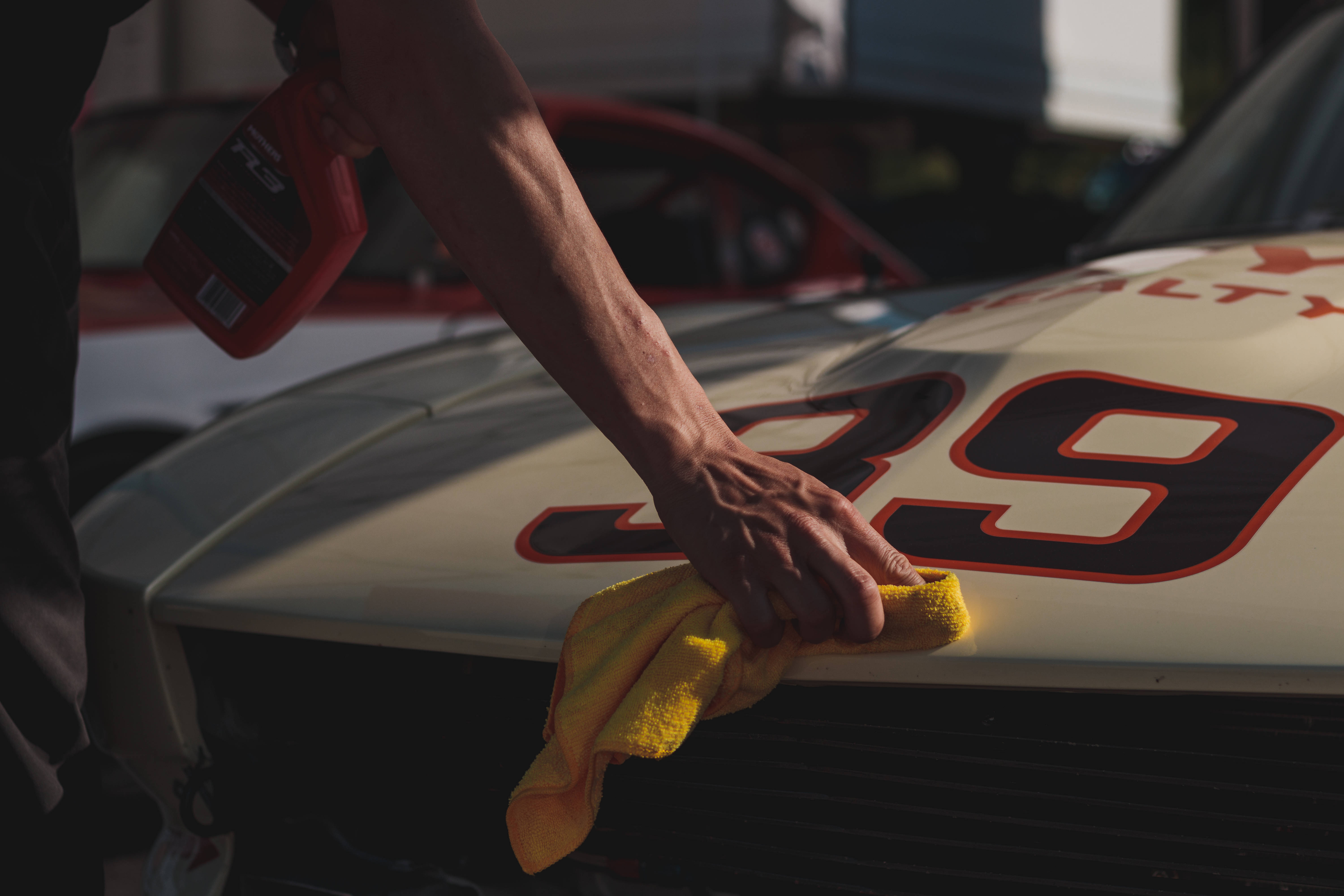 Racing 桌布 壁紙 — 一個人在溫暖的陽光下，用黃色布仔細擦拭一輛白色賽車的引擎蓋，車上印有39號。