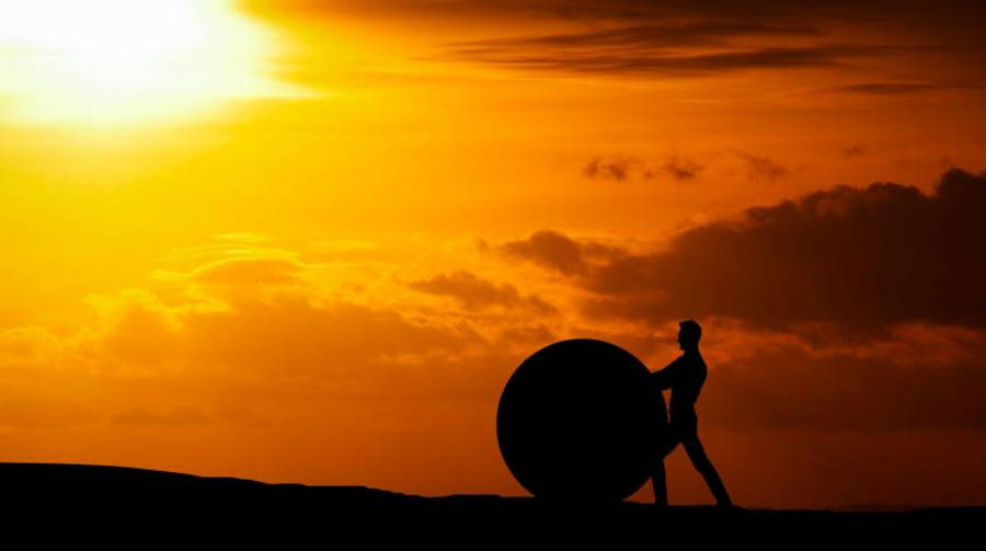 Motivation 桌布 壁紙 — 一個人在火紅的日落時分將一個巨大的球體推過地平線的剪影。