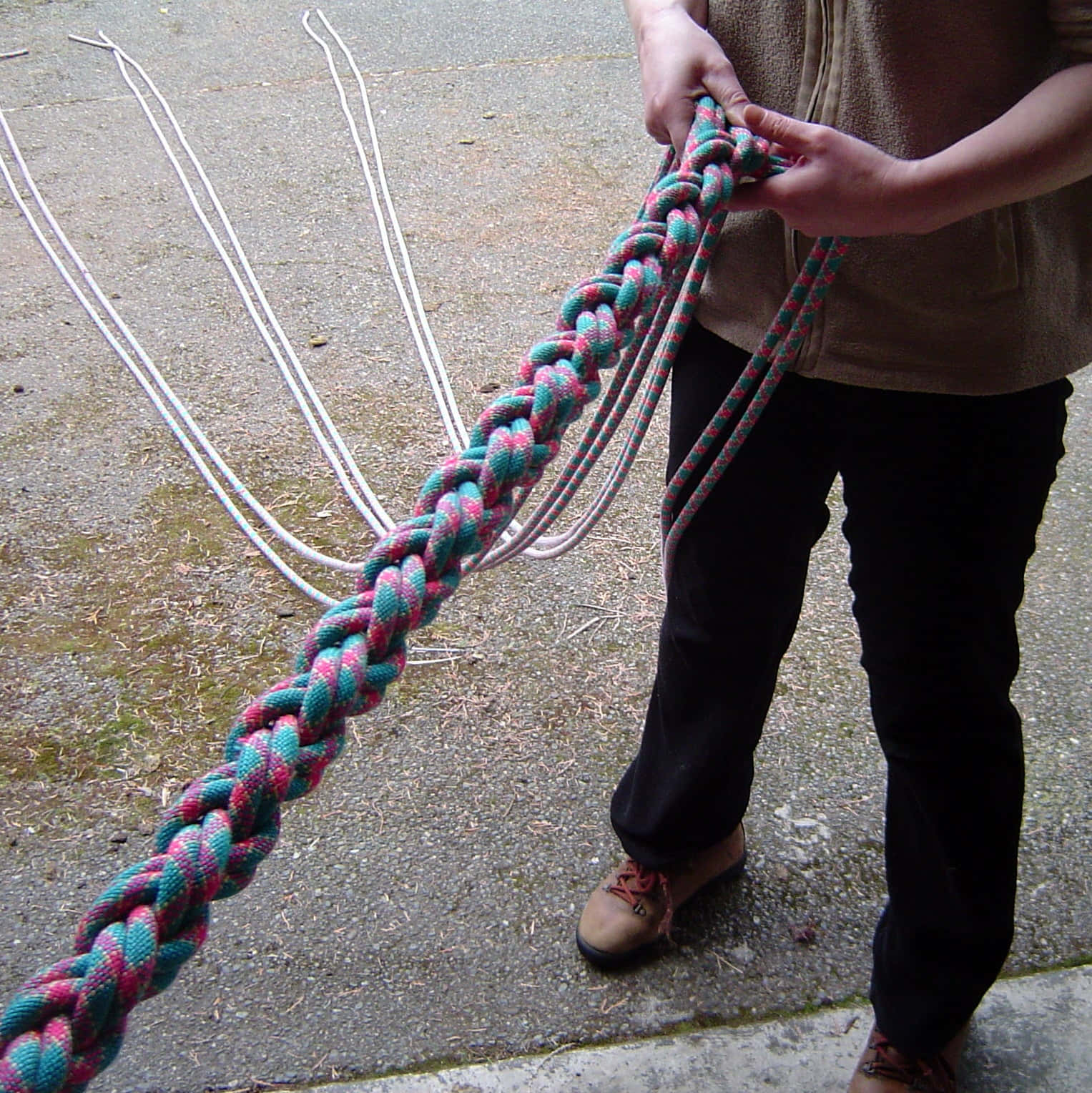 rope 桌布 壁紙 — 一個人在灰色混凝土背景前，握住一條由青綠色和粉紅色繩股編成的粗辮繩。