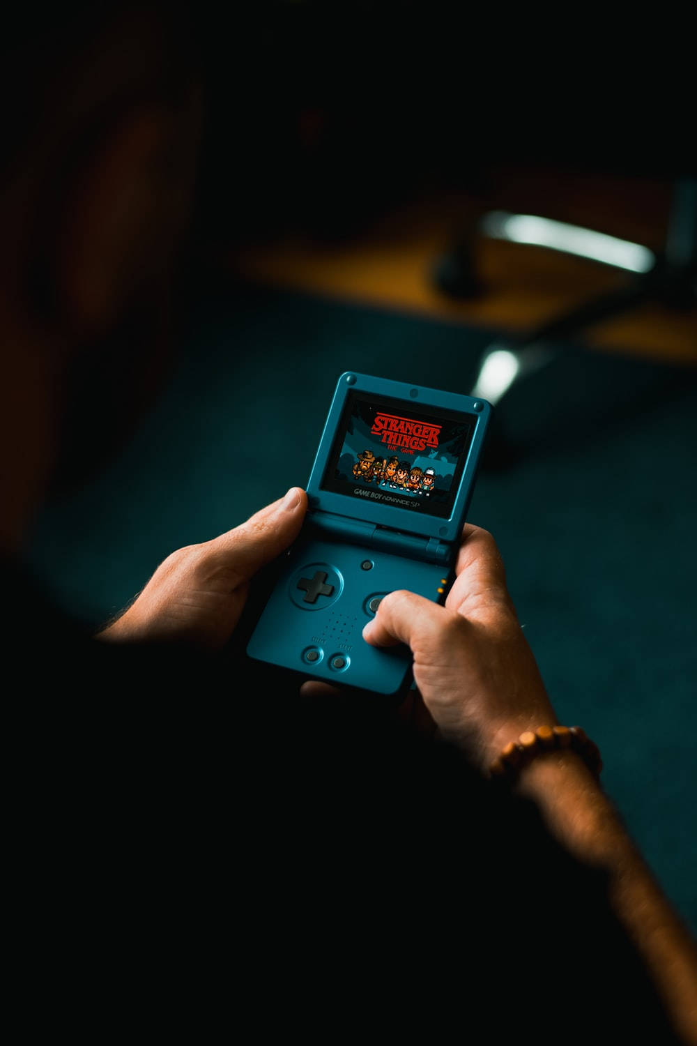 game 桌布 壁紙 — 一個人在燈光昏暗的房間裡手持一部顯示《怪奇物語》遊戲的藍色掌上型遊戲機。
