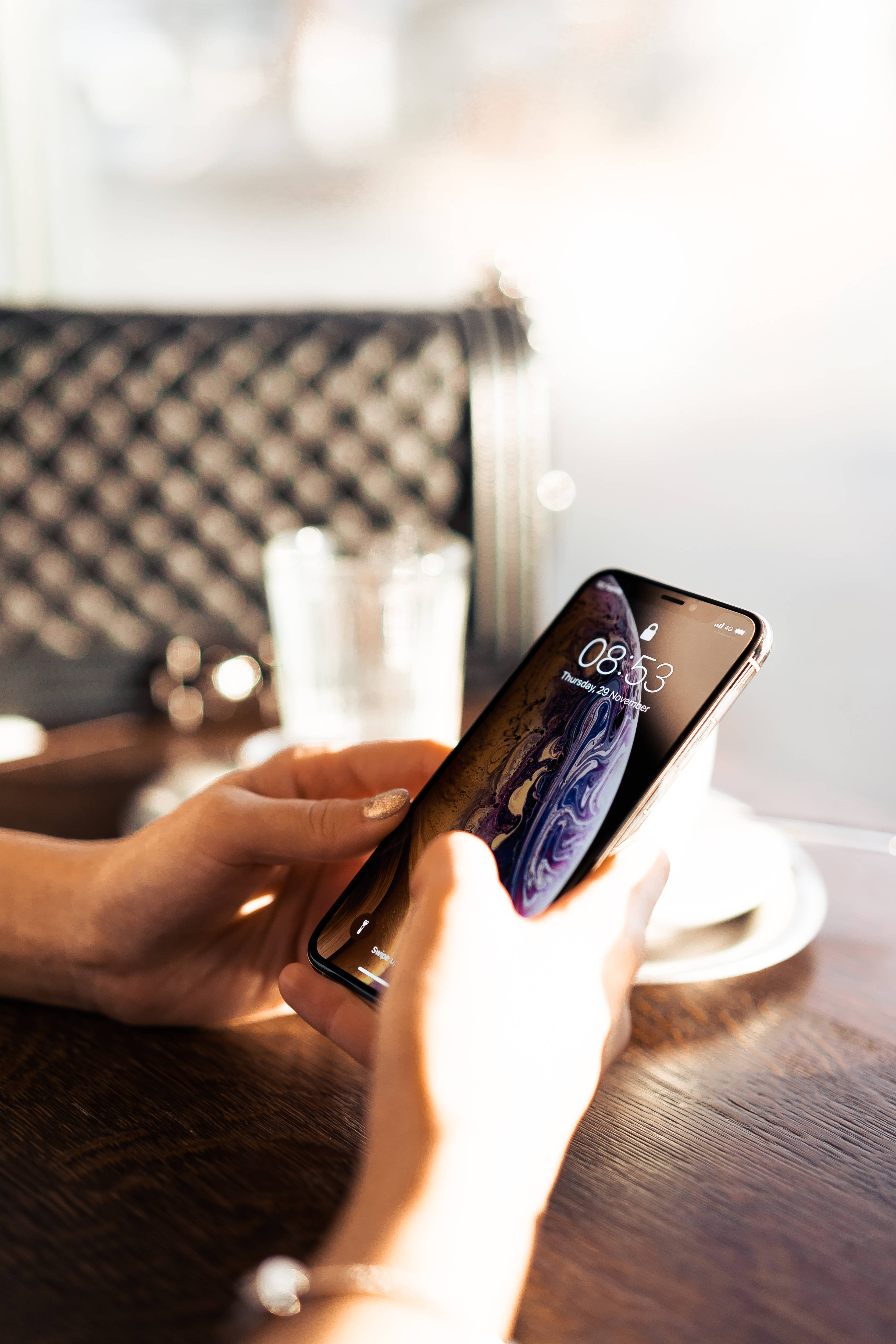 phone girl 桌布 壁紙 — 一個人在燈光柔和的咖啡廳木桌上，手持顯示旋轉宇宙桌布的智慧型手機。
