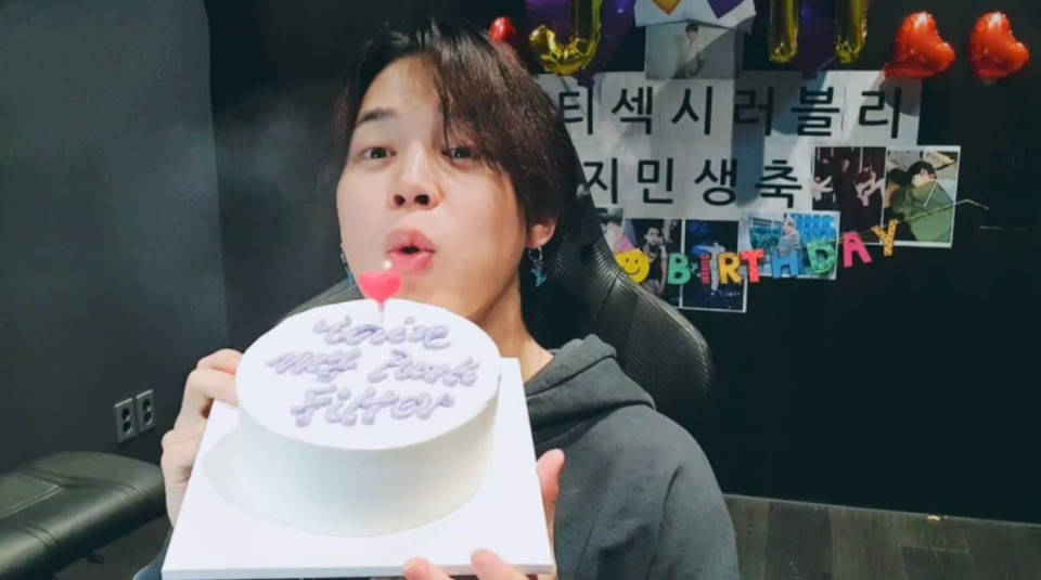 BTS 智旻 桌布 壁紙 — 一個人在白色生日蛋糕上吹熄蠟燭，周圍是節日裝飾和照片。