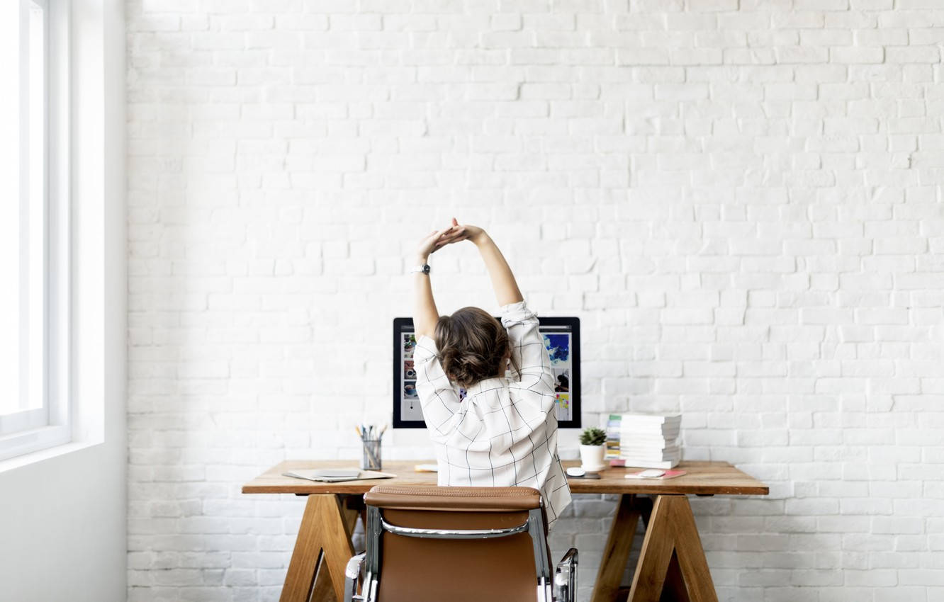 Working 桌布 壁紙 — 一個人在白色磚牆的明亮簡約辦公室中，在木桌上將手臂伸展過頭。