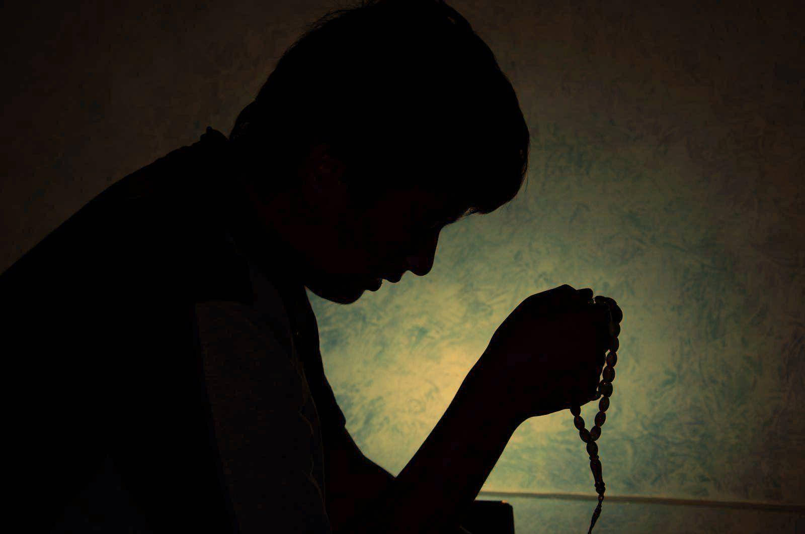 Prayer 桌布 壁紙 — 一個人在祈禱中手持玫瑰經，背對有紋理的牆壁，溫暖的背光照射下的剪影。