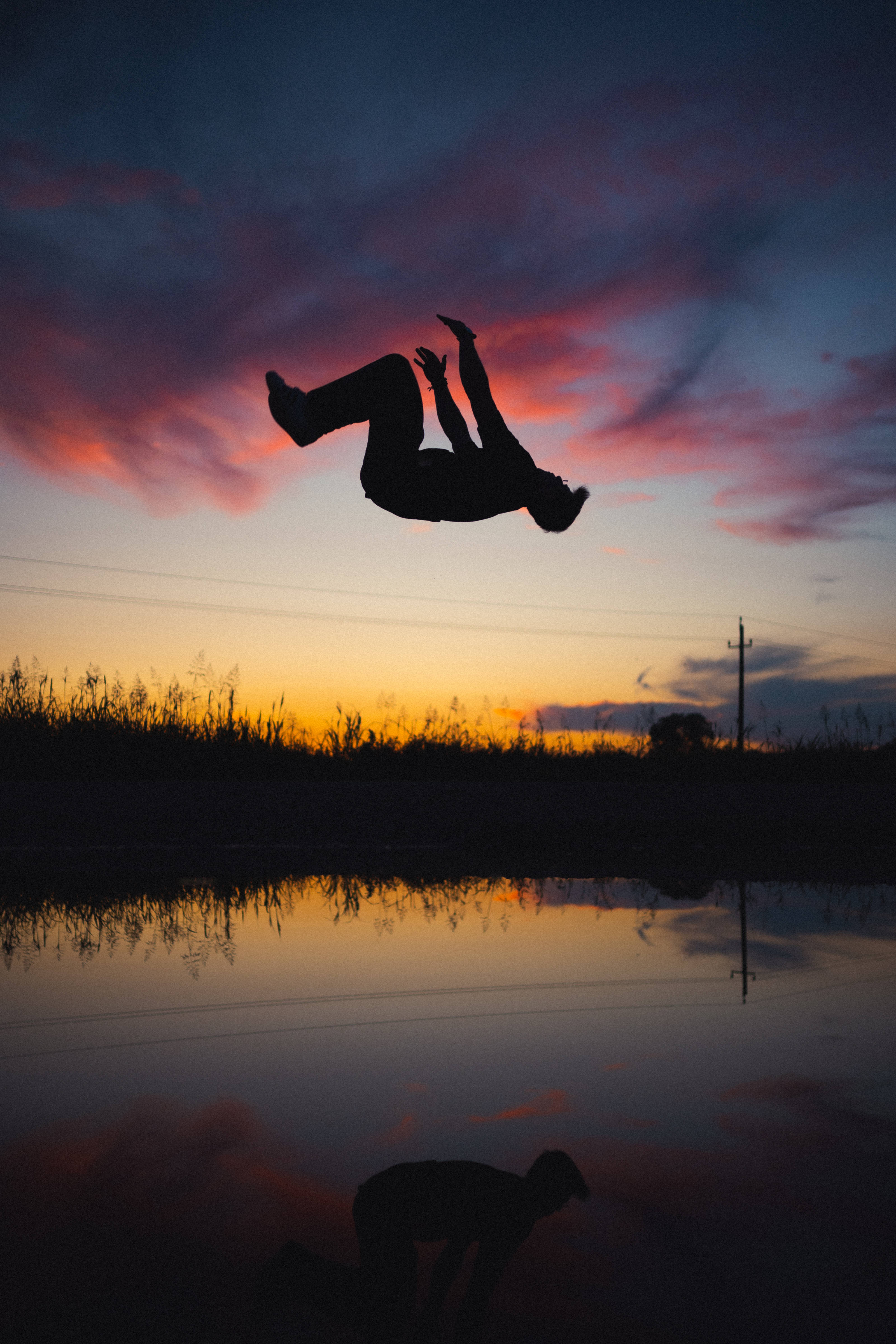 Parkour 桌布 壁紙 — 一個人在空中翻騰，背景是映照在平靜水面上的 vibrant 日落天空。