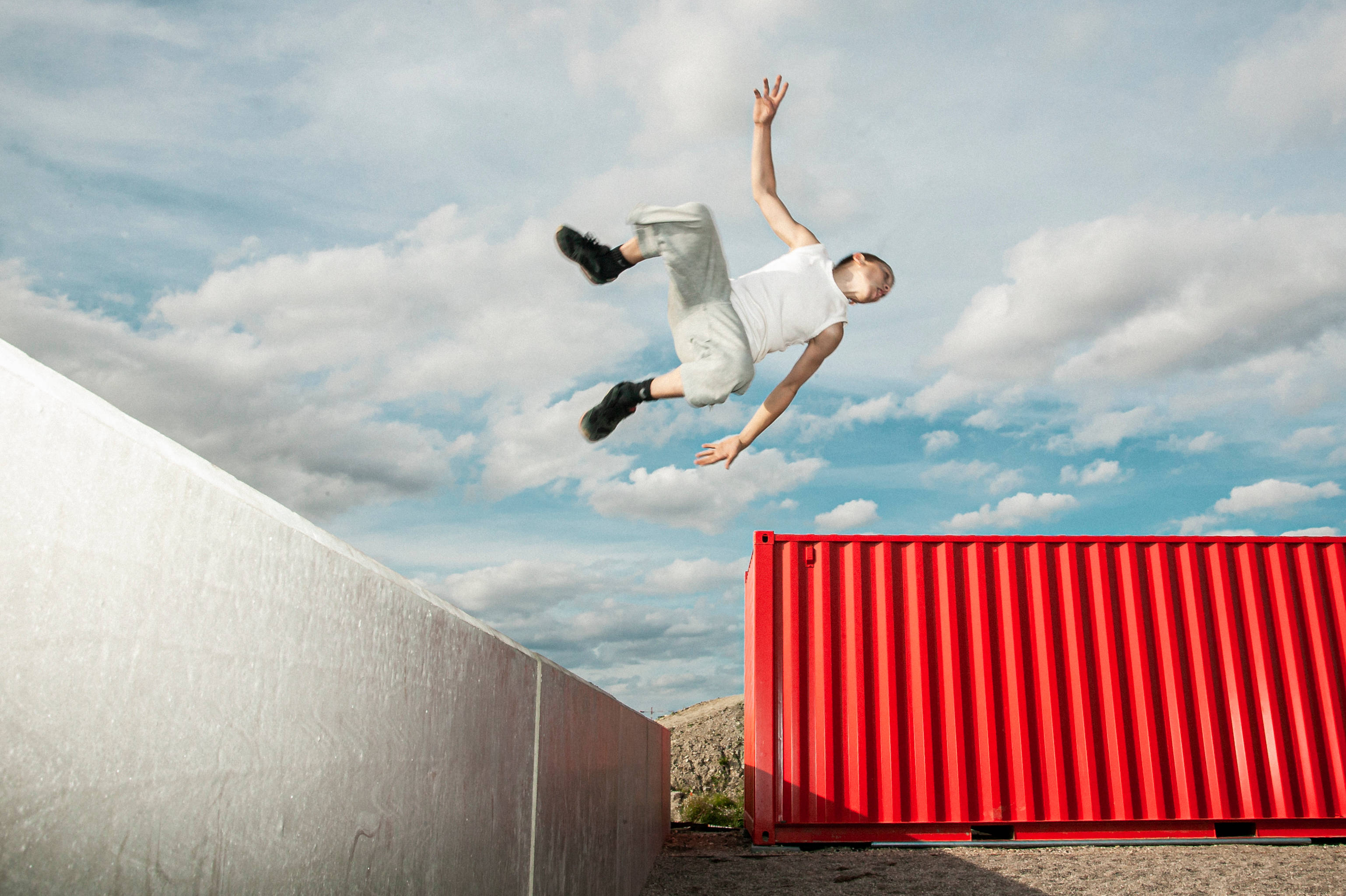 Parkour 桌布 壁紙 — 一個人在空中飛躍過一個紅色貨櫃，背景是藍天白雲。